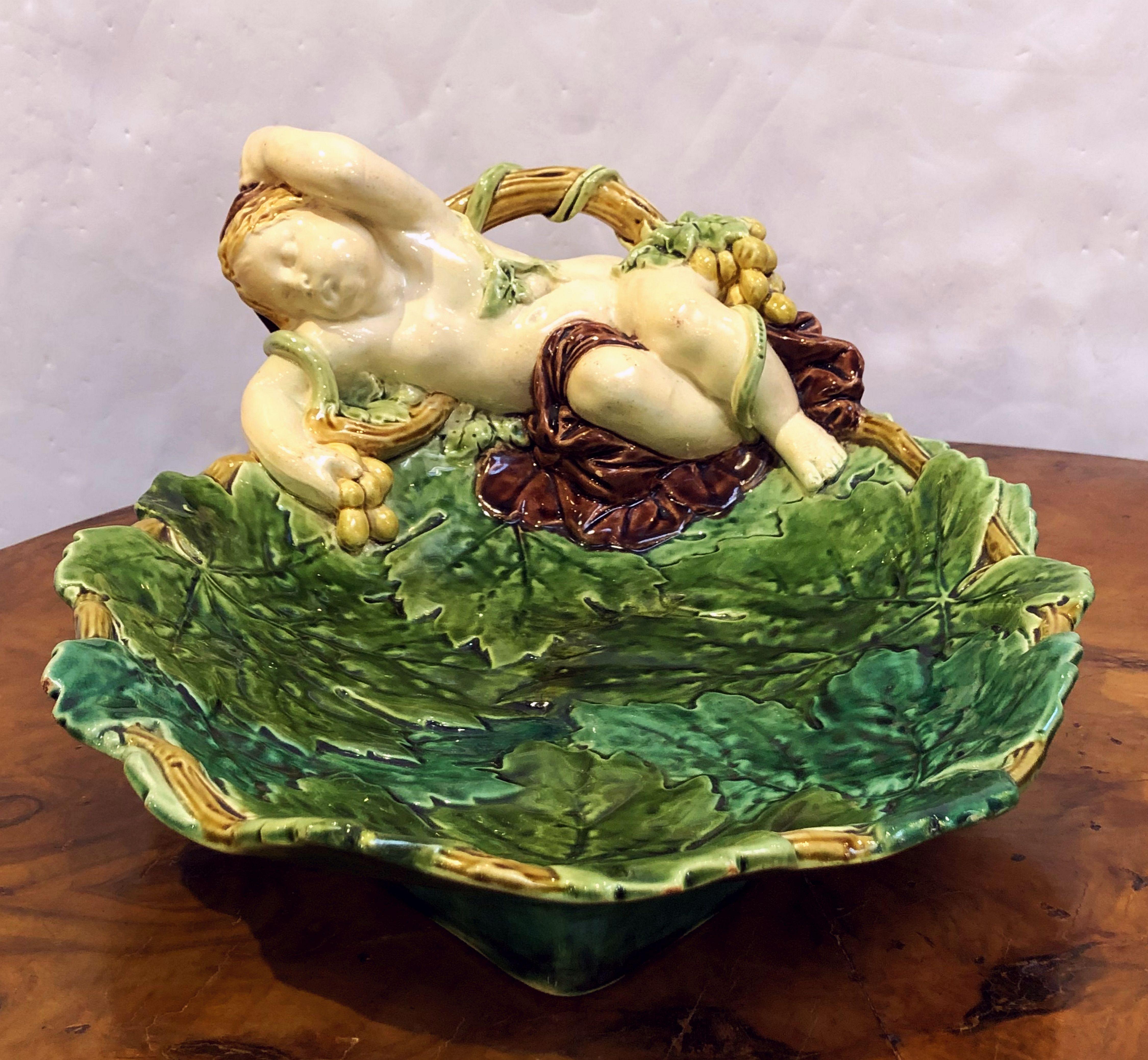 A fine Majolica serving platter or bowl by the celebrated English pottery firm, Minton.
Featuring a design of a recumbent cherub or child clutching grapes upon a bed of grape leaves. 
Impressed registration and makers marks on the base.