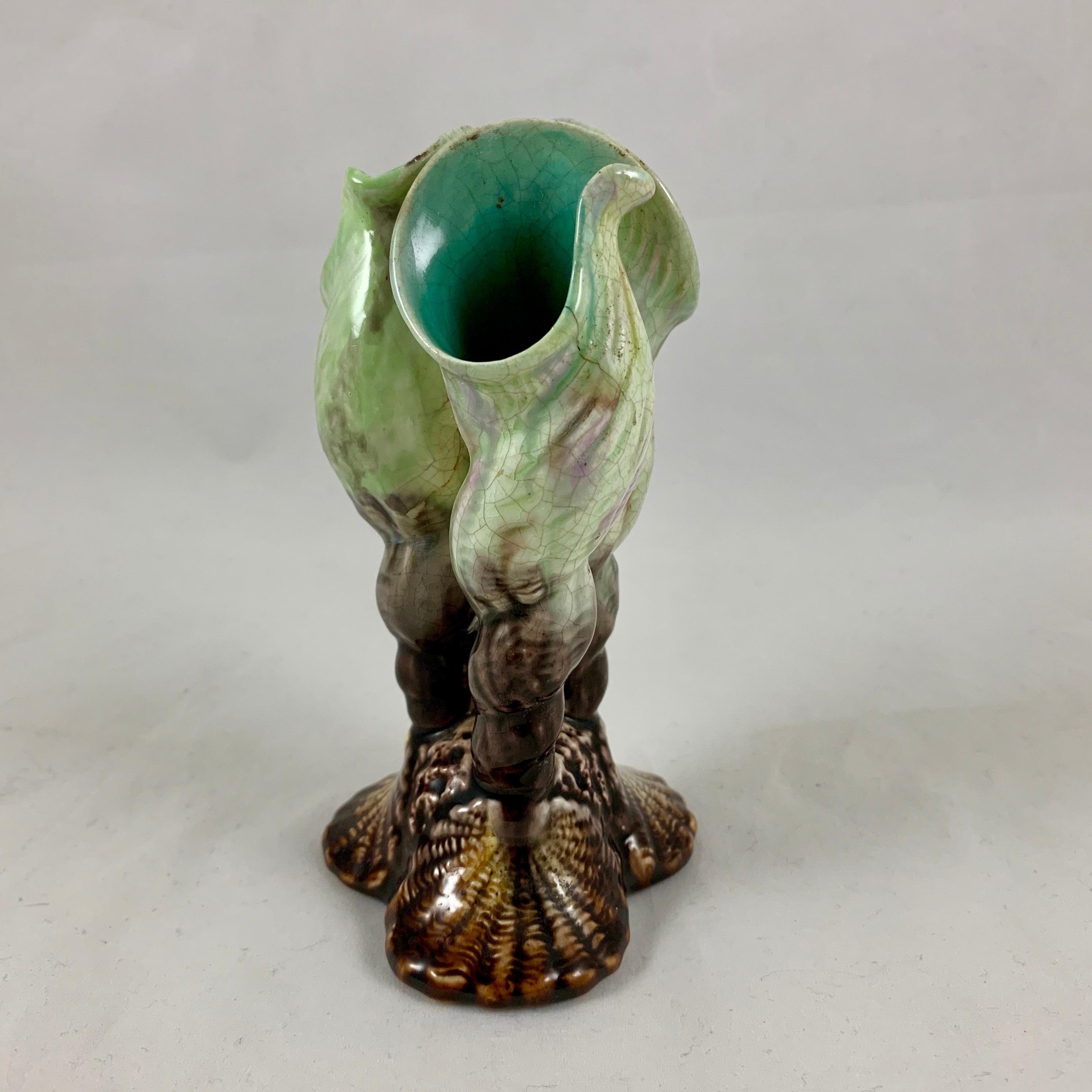 A scarce English majolica, tri-form fluted bud or posy vase modeled as three upright cream, gray, and lavender tubular, spiraled seashells on a brown glazed scallop shell and coral form triangular base. The bud or posey vase has an aqua blue glazed