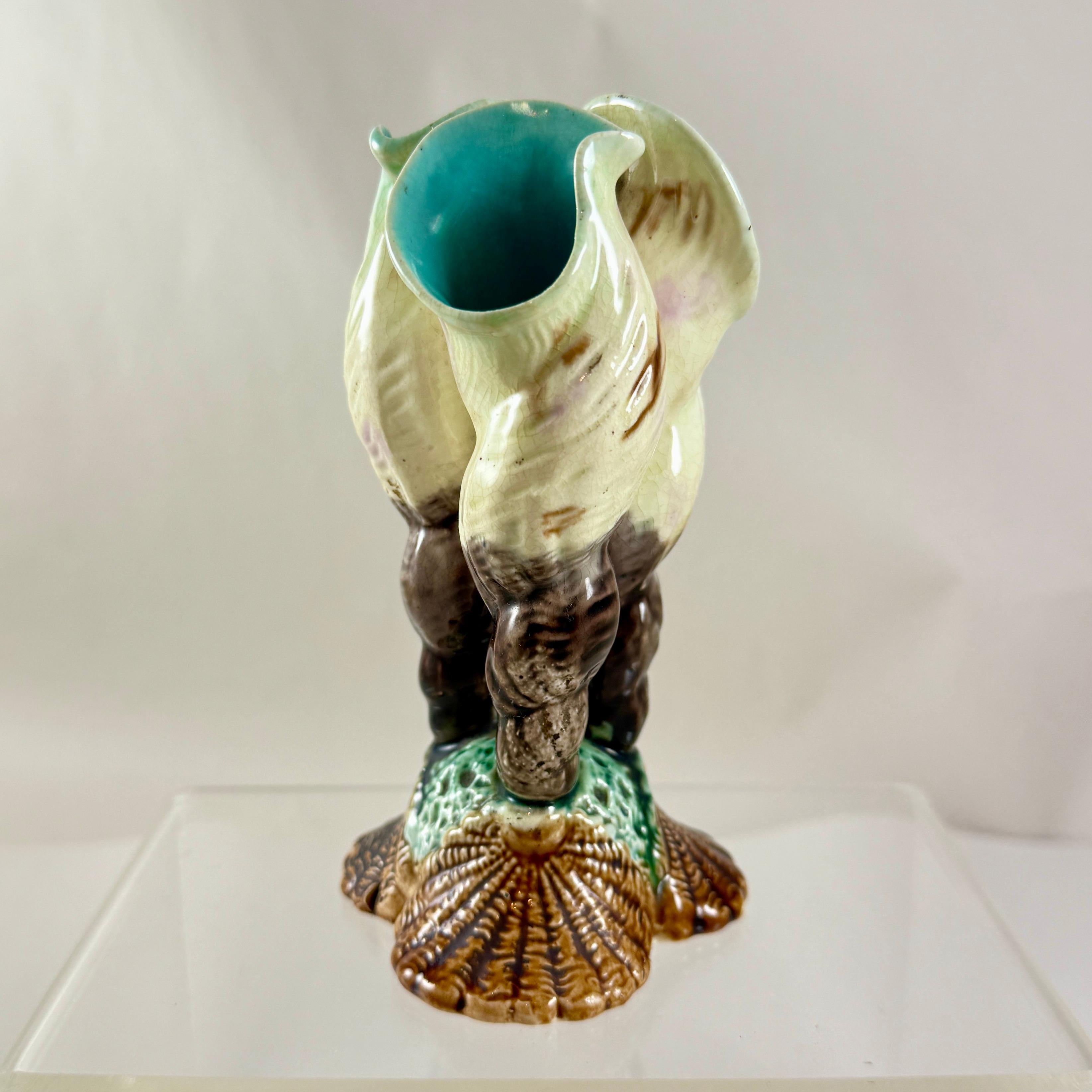 Uno scarso vaso in maiolica inglese, a tre forme di boccioli scanalati o pose, modellato come tre montanti color crema, grigio e con accenni di lavanda,  conchiglie tubolari e a spirale su una base triangolare a forma di conchiglia smerlata e