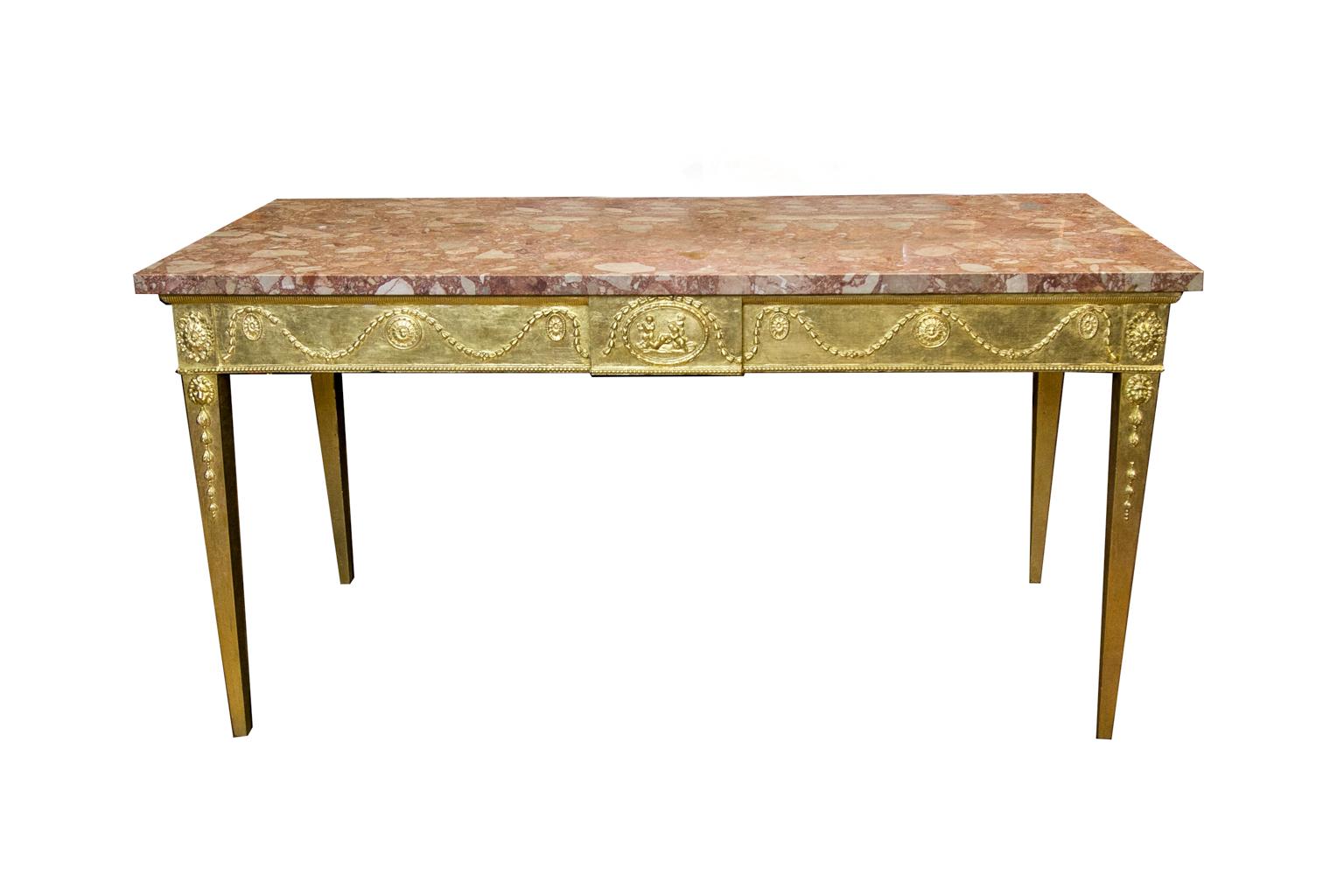 The top of this gilt console table has a straight rectangular marble (later). The apron has carved bellflower swags on three sides and a center cartouche with children playing. The lower apron has a repeating carved bead. The legs have a carved