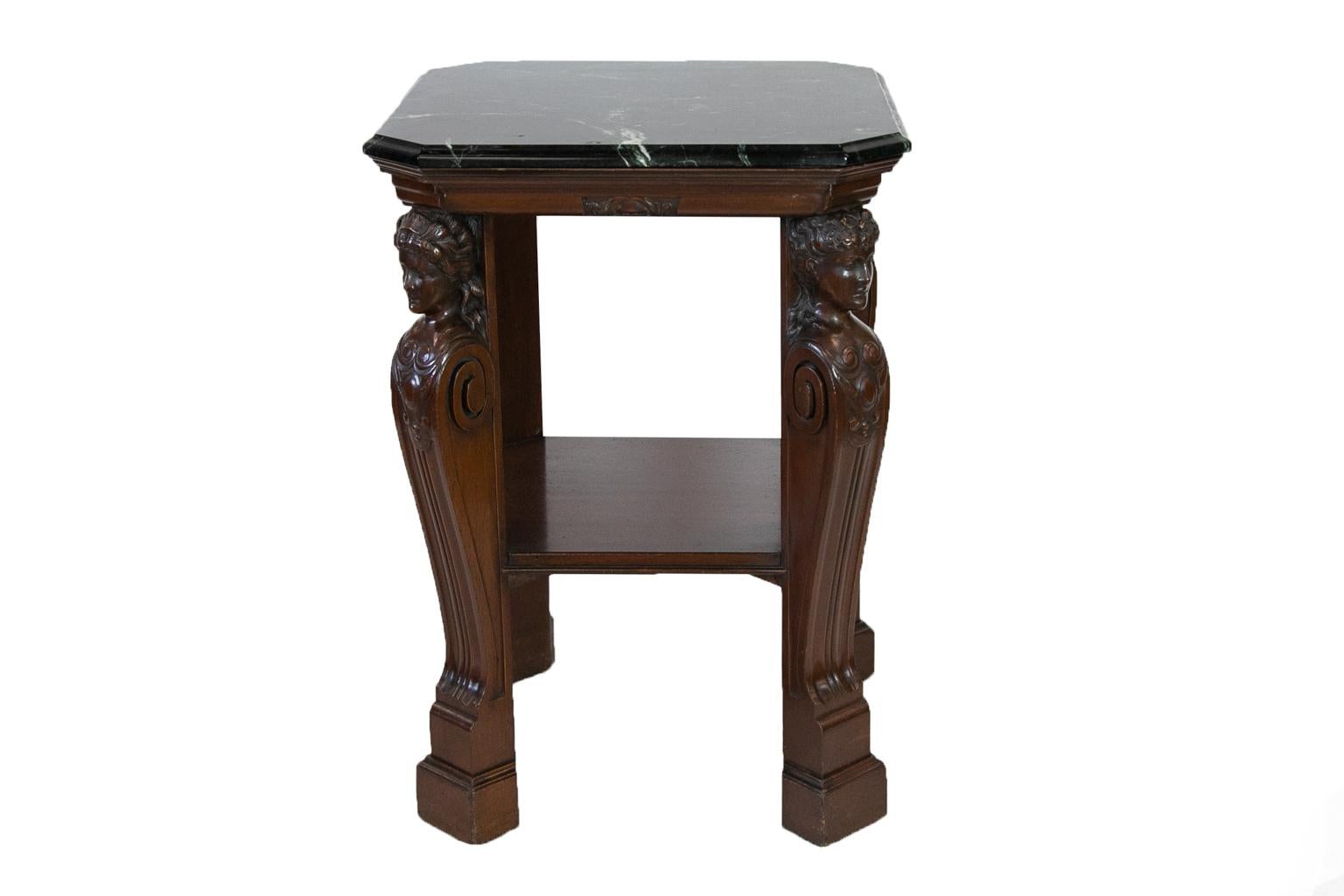 English marble-top center table is solid mahogany and has carved female busts at the top of the legs, which taper down with carved shaping, terminating in rectangular molded plinth feet.
