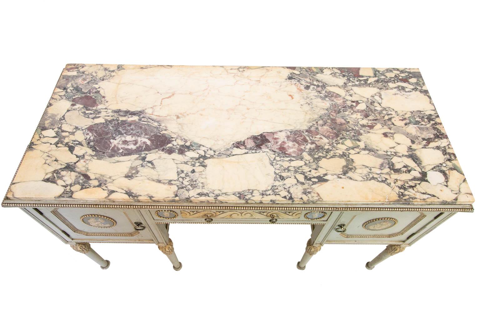 This marble top console table is painted mahogany. The top is bordered by repeating bead molding. The doors and drawers have applied jasperware panels with classical figures and cherubs surrounded by beadwork frame. The center door has stylized left