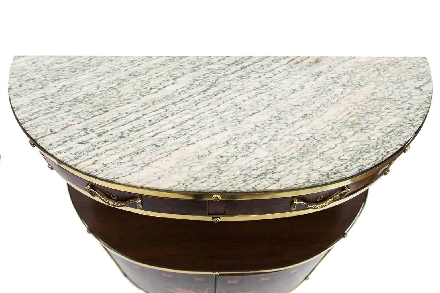 English Marble Top Demi Lune Server, the doors are beautifully inlaid with satinwood swans drinking from a flowing water fountain. The edges have heavy cast brass moldings with crotch mahogany throughout.


