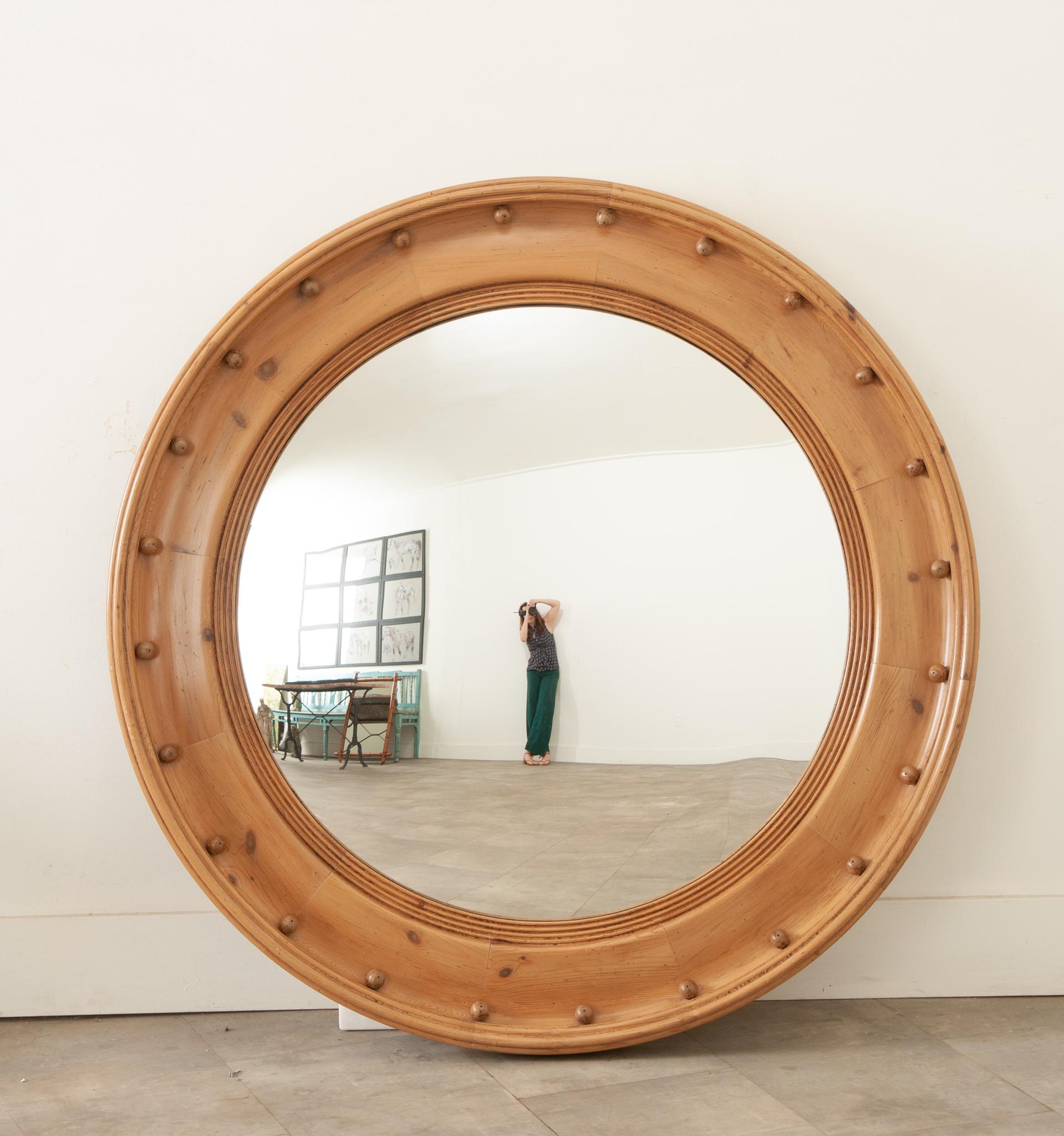 A massive English pine convex bullseye mirror with petite spheres and natural finish. Created in England during the 19th century, this stylish circular mirror features a central convex mirror plate reflecting and distorting images beautifully,