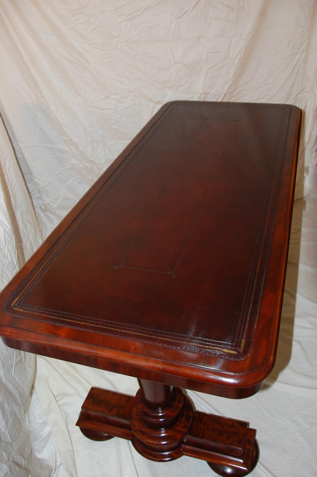 English Early Victorian mahogany leather top writing, library, or sofa table with bold pedestal ends. This simple yet handsome table has tapered, turned pedestal ends which are centered on a Classic mahogany platform supported by flattened bun feet.