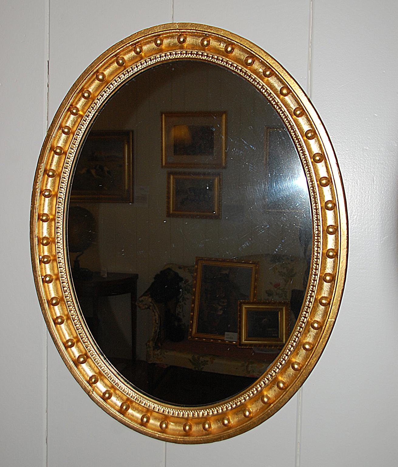 English mid-19th century carved oval gold leaf mirror with balls in its concave molding, leaf motif next to plate mirror. It is unusual to have an oval mirror with balls surrounding the edge, usually this is reserved for round convex mirrors. The