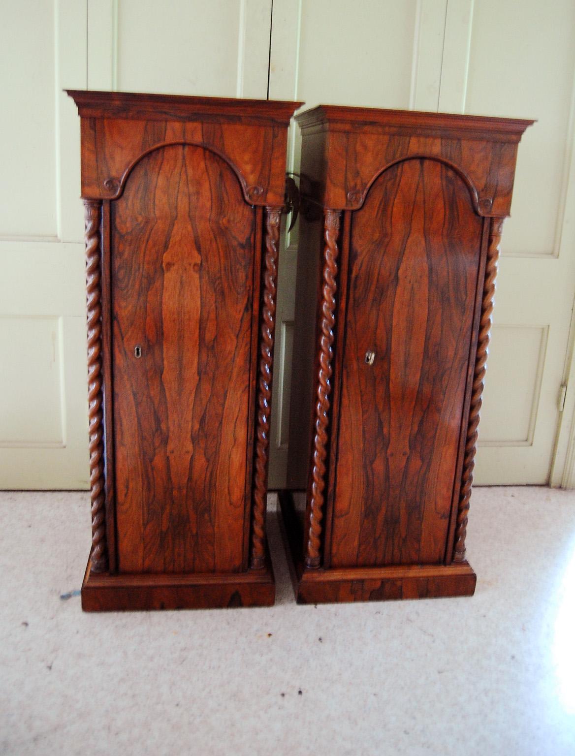 English pair of rosewood pedestal cabinets with barley twist carved columns, cathedral arched hinged doors, interior shelves on plinth bases. The graining of the rosewood is stupendous with book matched veneers to the front of each pedestal. These