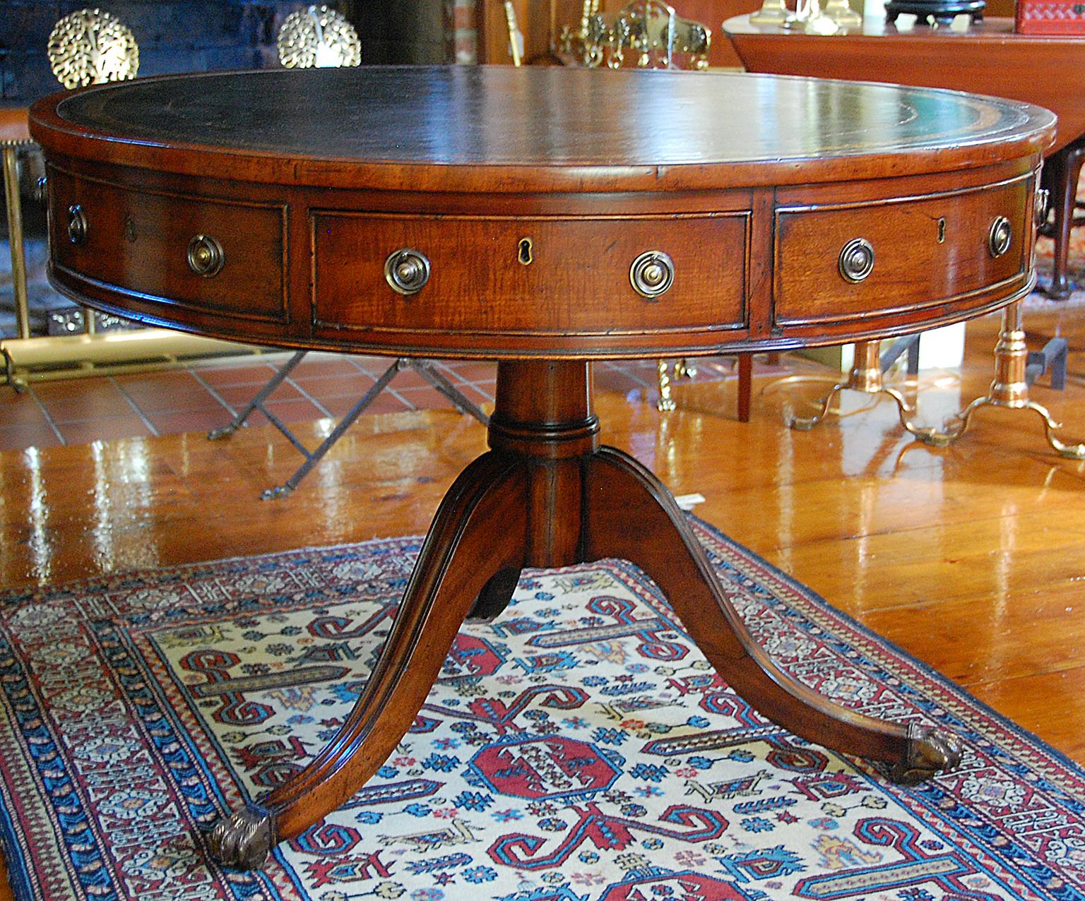 English Regency style, mid-19th century mahogany drum table, reeded down swept legs ending in cast brass paw casters, turned center pedestal, rich green hand dyed and gold tooled full leather inlaid top. Three working drawers, three sham drawers. At