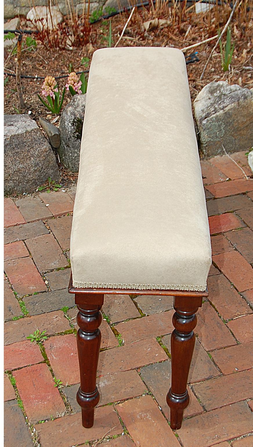 English mid-19th century upholstered bench with turned mahogany legs, and mahogany small molding to seat edge. The newly upholstered bench has a fawn colored ultrasuede fabric. At only 44 inches long this versatile bench can find a home in most