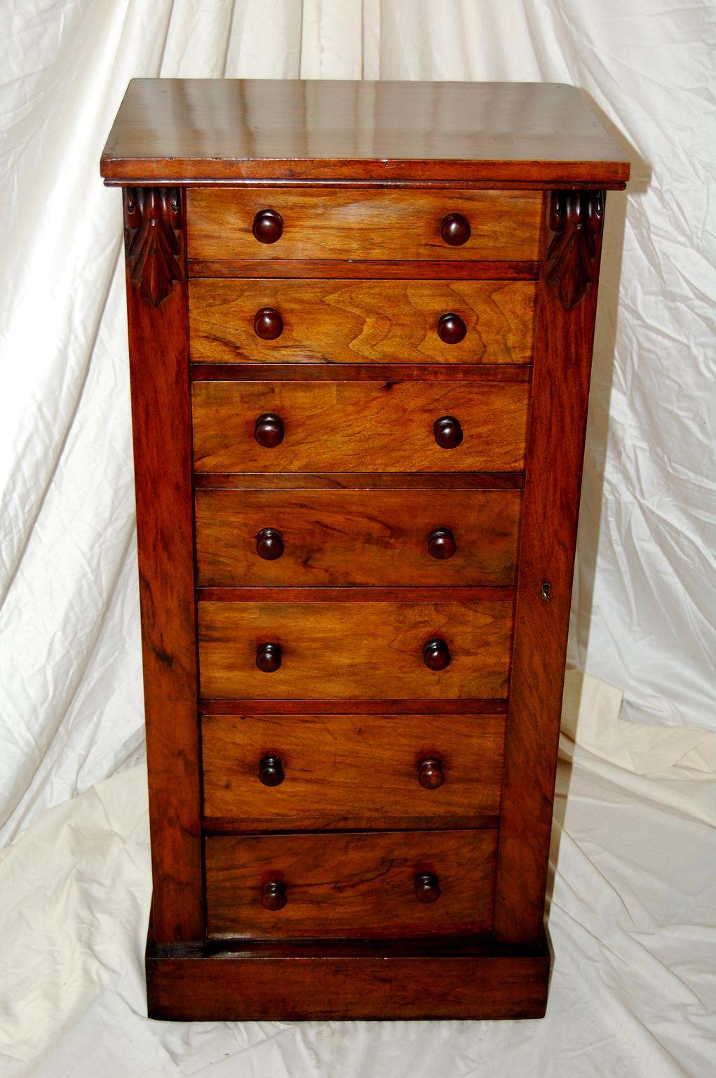 English walnut Wellington chest of seven graduated drawers. The right hand front frame of the chest is hinged and covers the right hand edge of the drawers by a small amount; when this is locked all of the drawers are locked at once; a device