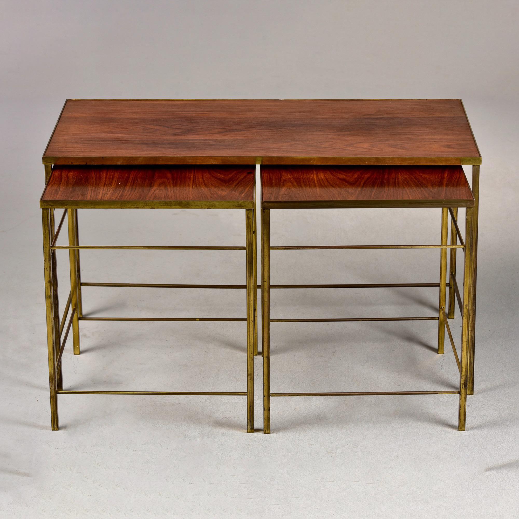 Found in England, this circa 1960s set of three stacking tables feature brass frames and what appears to be teak table tops. One larger table with two smaller tables that fit below. No maker’s marks found. Measurements shown are for the larger