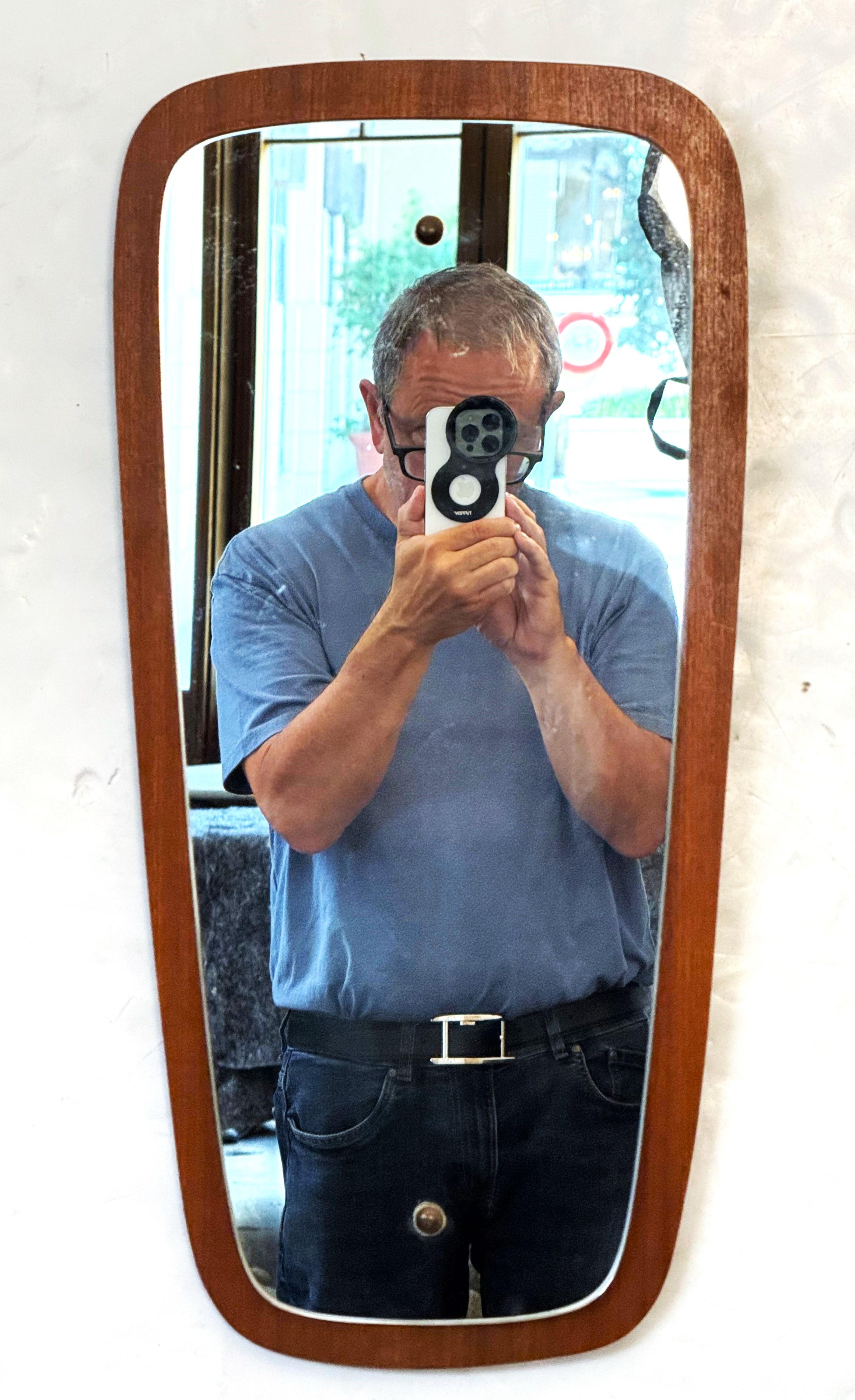 Un beau miroir mural rectangulaire anglais présentant un design moderne du milieu du siècle, avec un miroir monté sur un support en bois de teck.

Dimensions : H 23 in x 11 1/8 in x D 5/16 in