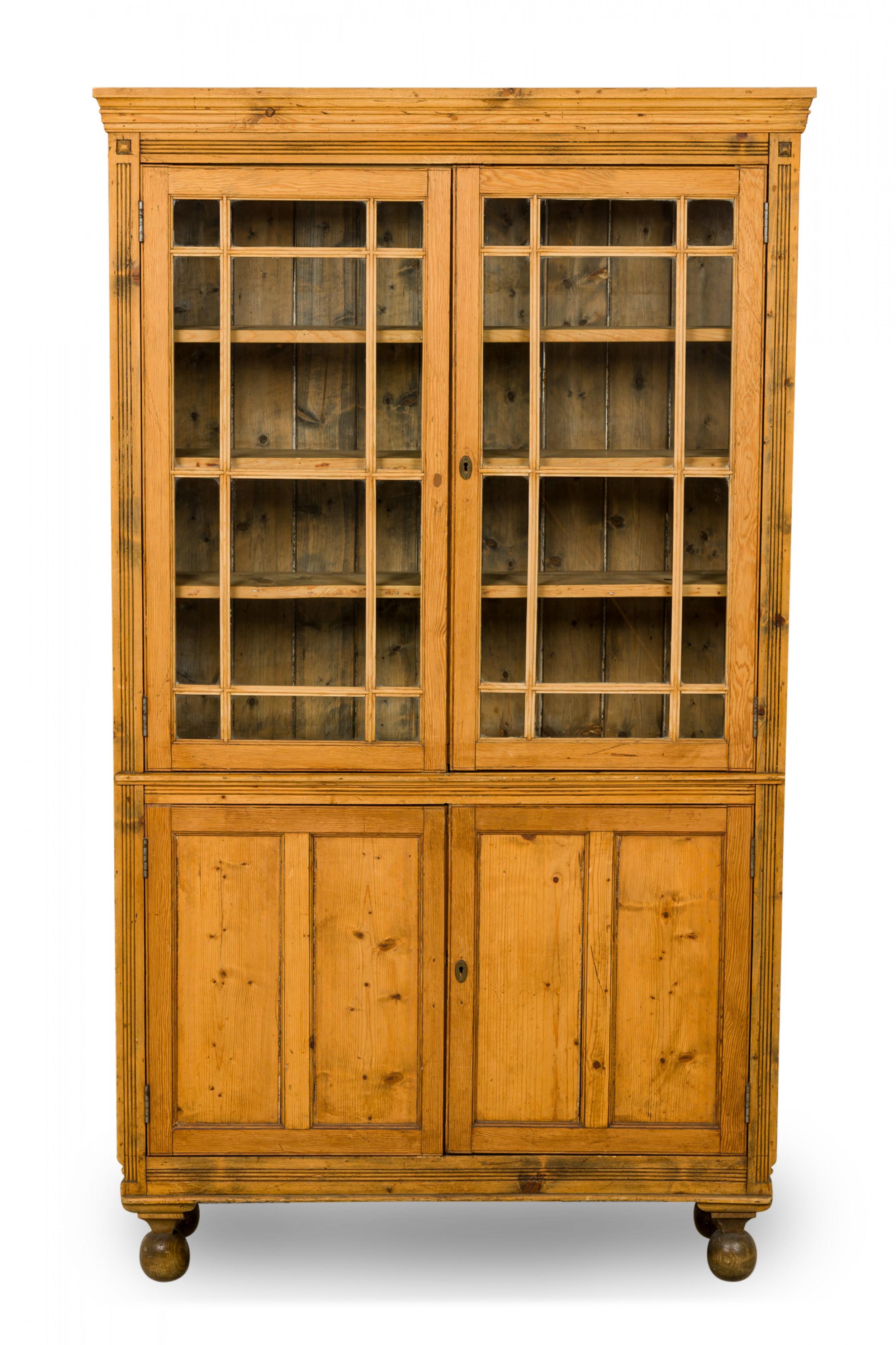 English mid-century breakfront pine wood hutch with an upper cabinet containing three wooden shelves with breakfront glass doors above a lower enclosed two door cabinet compartment containing two shelves, with carved fluted and medallion detail