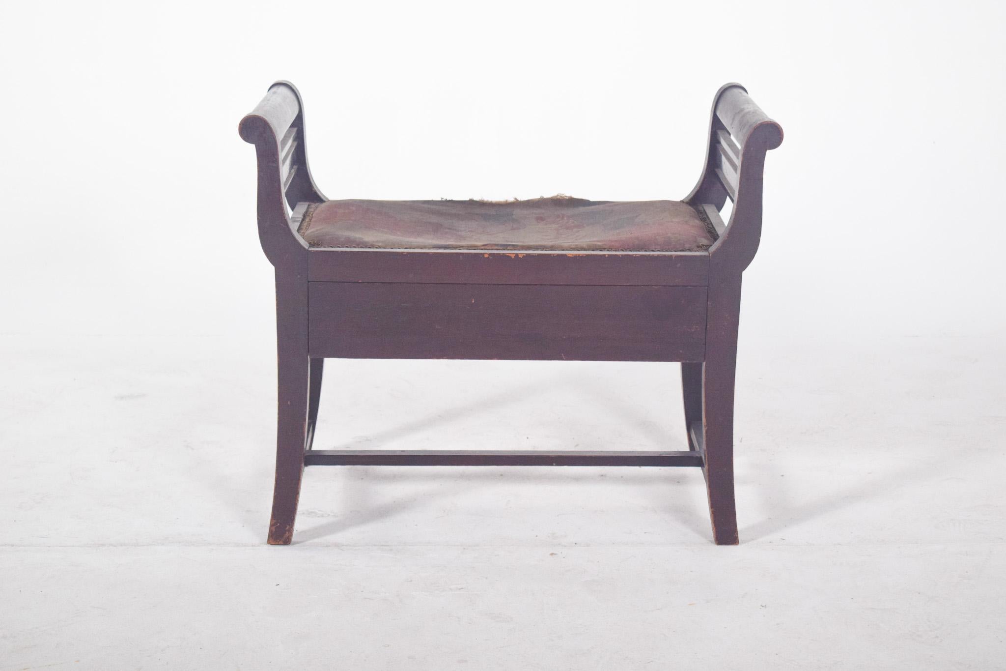 Tabouret avec tiroir.  De lignes droites, avec de légères courbes au niveau des accoudoirs, il est doté d'une assise rembourrée, actuellement en assez mauvais état, témoignant d'une utilisation prolongée. Les côtés ont des poutres horizontales en
