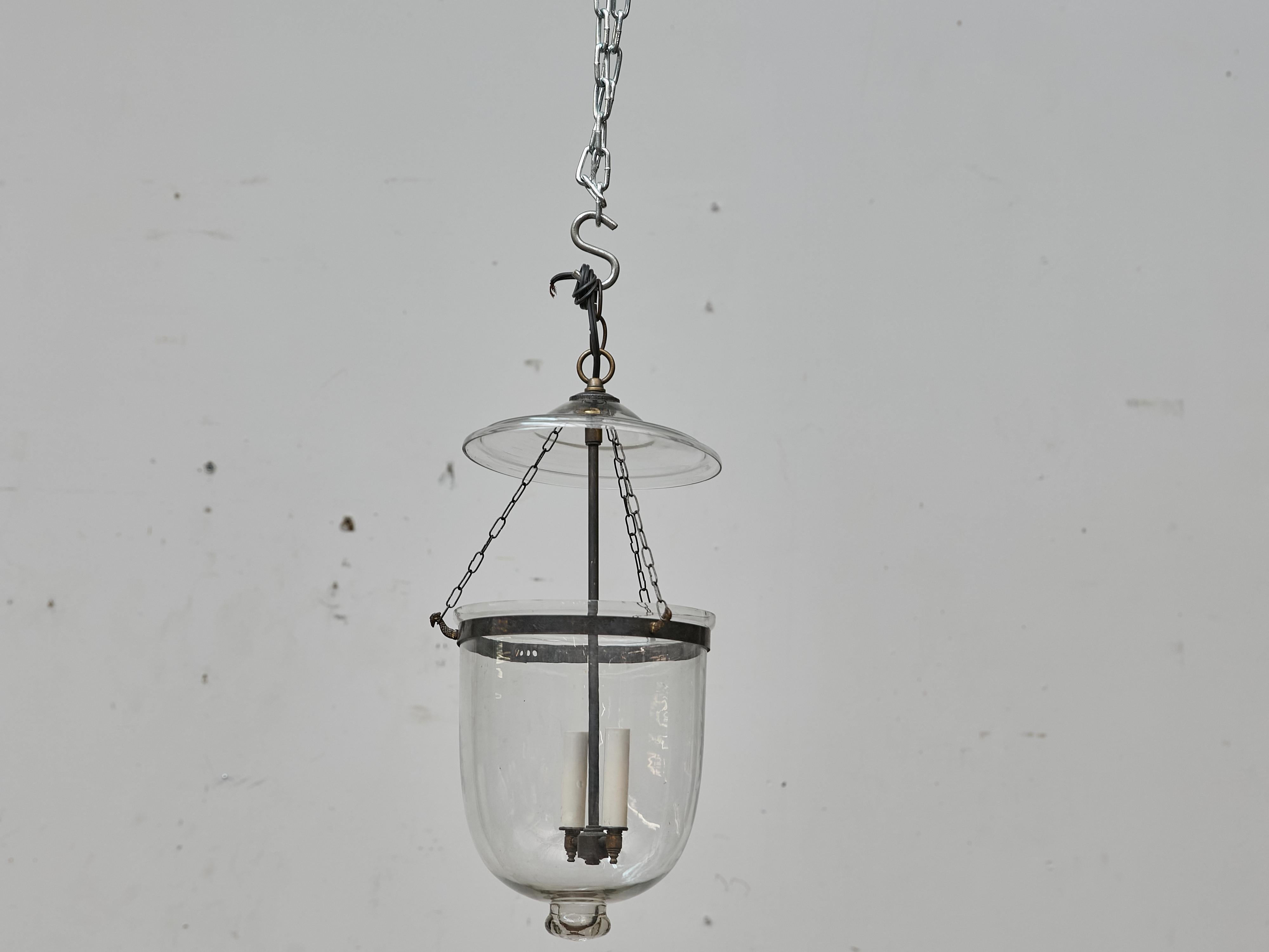 Una refinada linterna inglesa de campana de vidrio soplado transparente y metal pulido, de mediados del siglo XX. Esta luminaria compacta presenta un dosel de cristal abovedado suspendido por tres delicadas cadenas y un cuerpo clásico en forma de