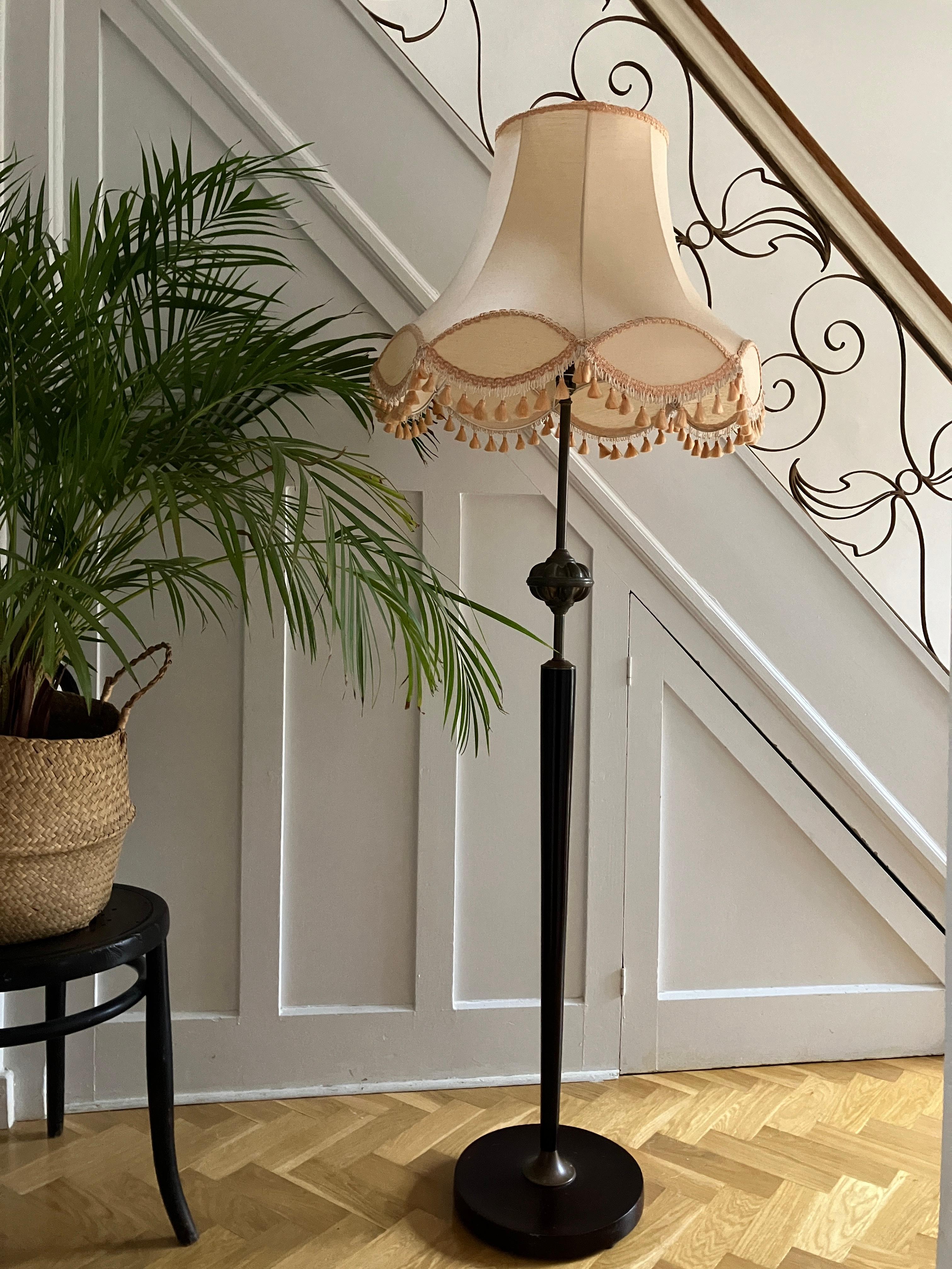Beautiful midcentury floor lamp from England. The lamp is made of brass and wood. The stand has an ebonized mahogany base with brass details and is topped by a slim brass bulb holder. The lamp is decorated with a stunning brass knot or a motif. It