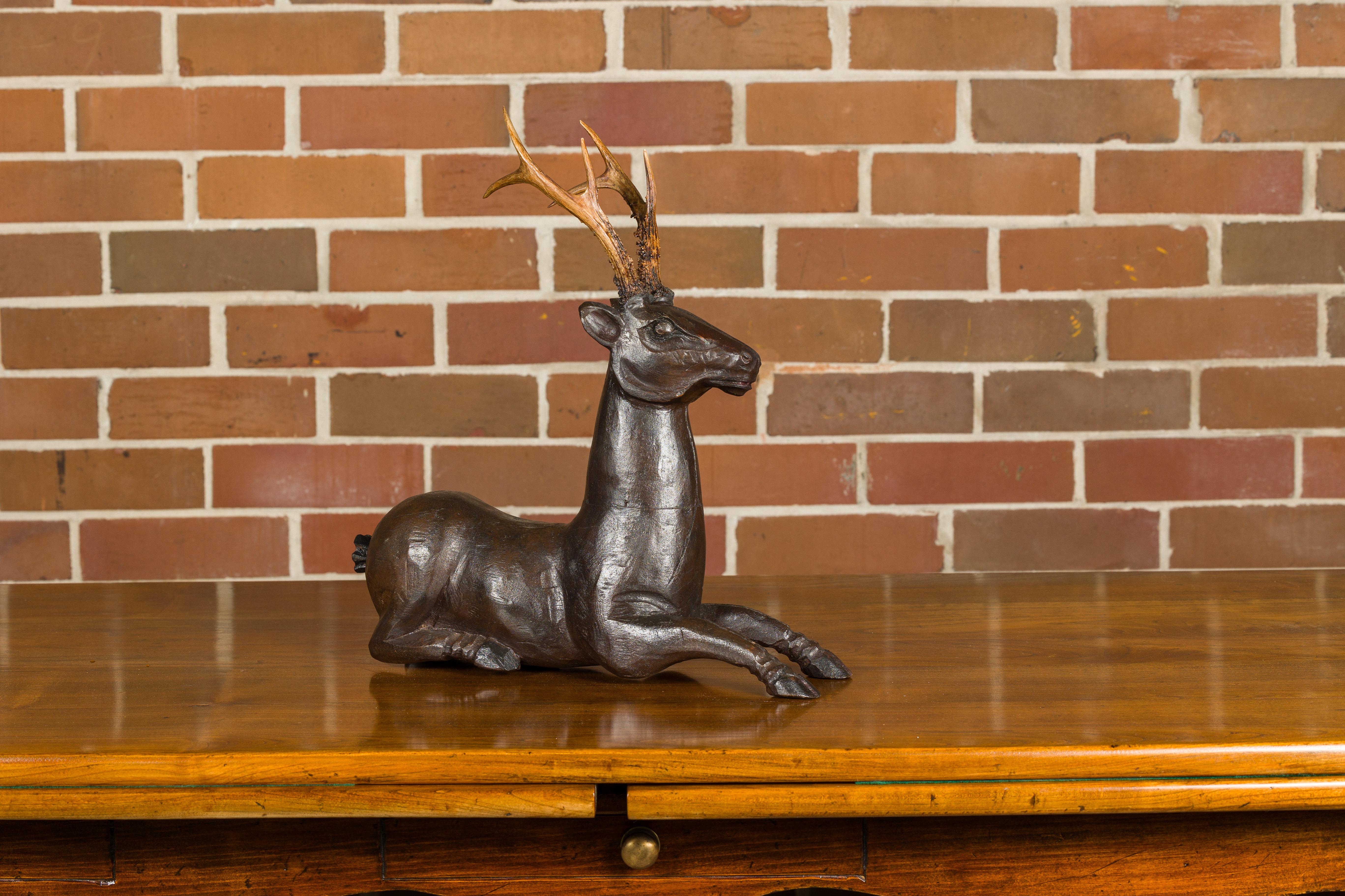 An English carved wooden reclining stag sculpture from the Midcentury period with real antlers. Elevate your interior with this captivating Midcentury English carved wooden reclining stag sculpture, a true testament to craftsmanship and artistry.