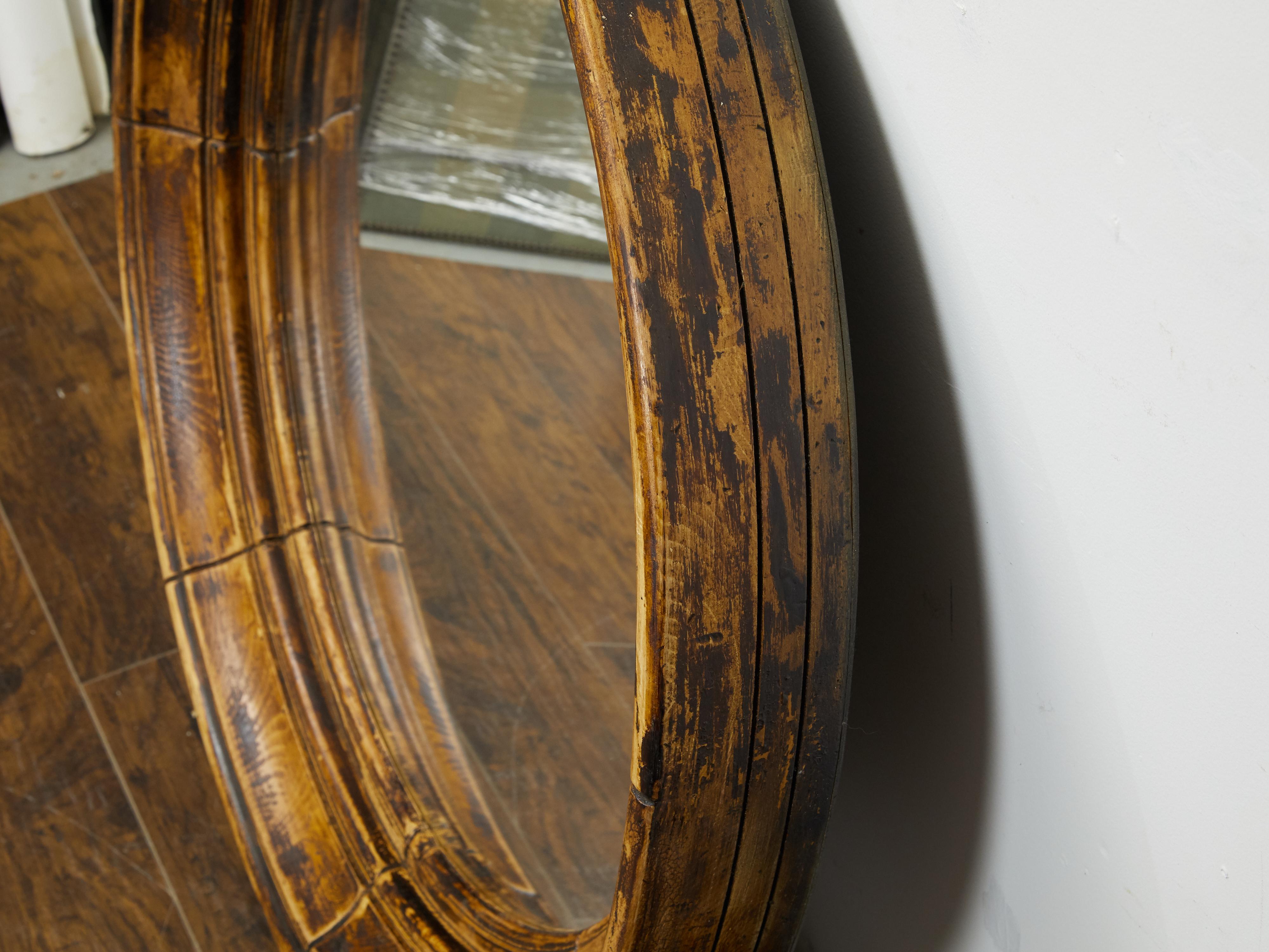 An English pine mirror from the mid 20th century, with distressed finish. Created in England during the midcentury period, this pine mirror charms us with its circular frame boasting a nicely weathered appearance. Made of radiating sections, this