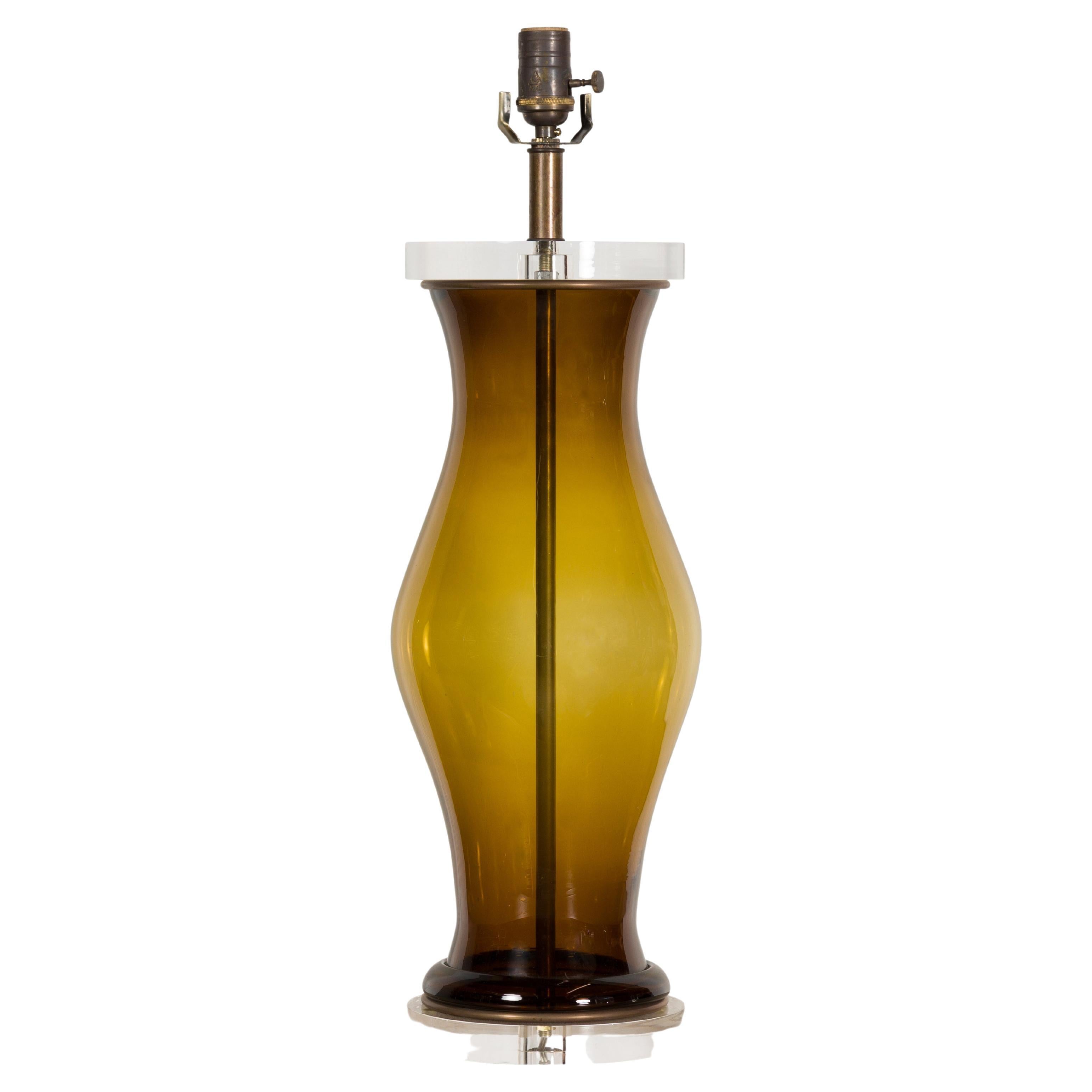 A Midcentury English dark amber glass table lamp with custom lucite base, rewired for the USA. Immerse yourself in the warm glow of sophistication with this Midcentury English dark amber glass table lamp. A radiant beacon of vintage charm and modern
