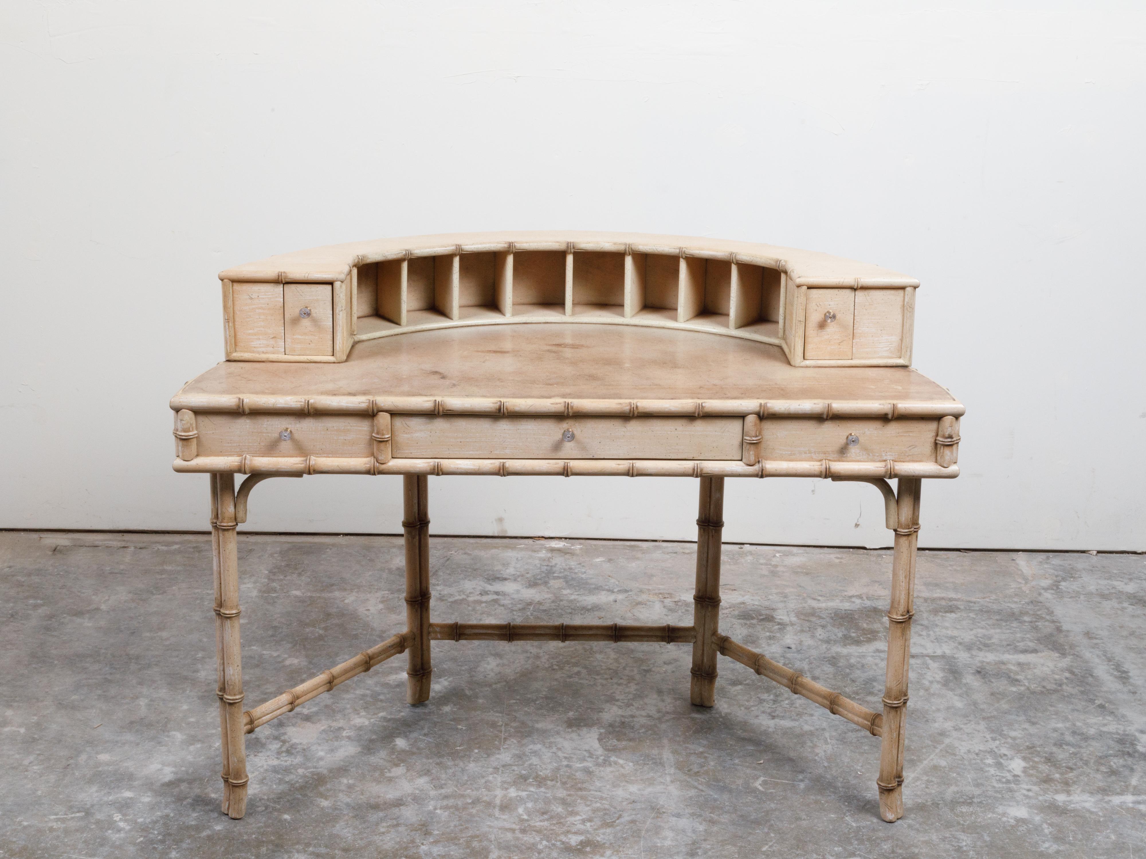 An English faux bamboo desk from the mid-20th century, with vellum top, semi-circular shelf and drawers. Created in England during the mid-century period, this desk features a semi-circular shelf with multiple compartments and side drawers, sitting