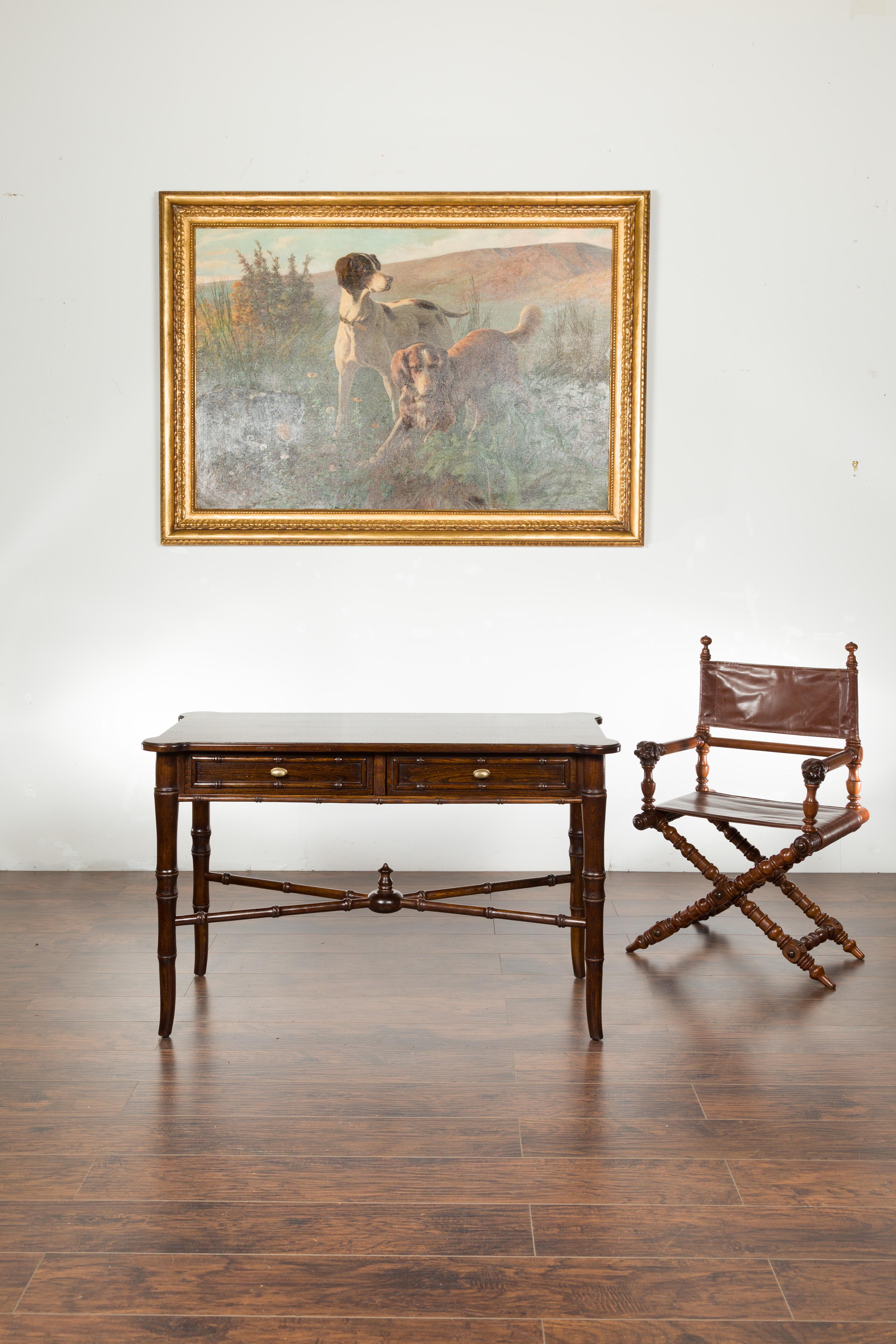 An English vintage faux bamboo walnut desk from the mid 20th century, with two drawers and cross stretcher. Created in England during the midcentury period, this walnut desk features a rectangular top with protruding rounded corners, sitting above