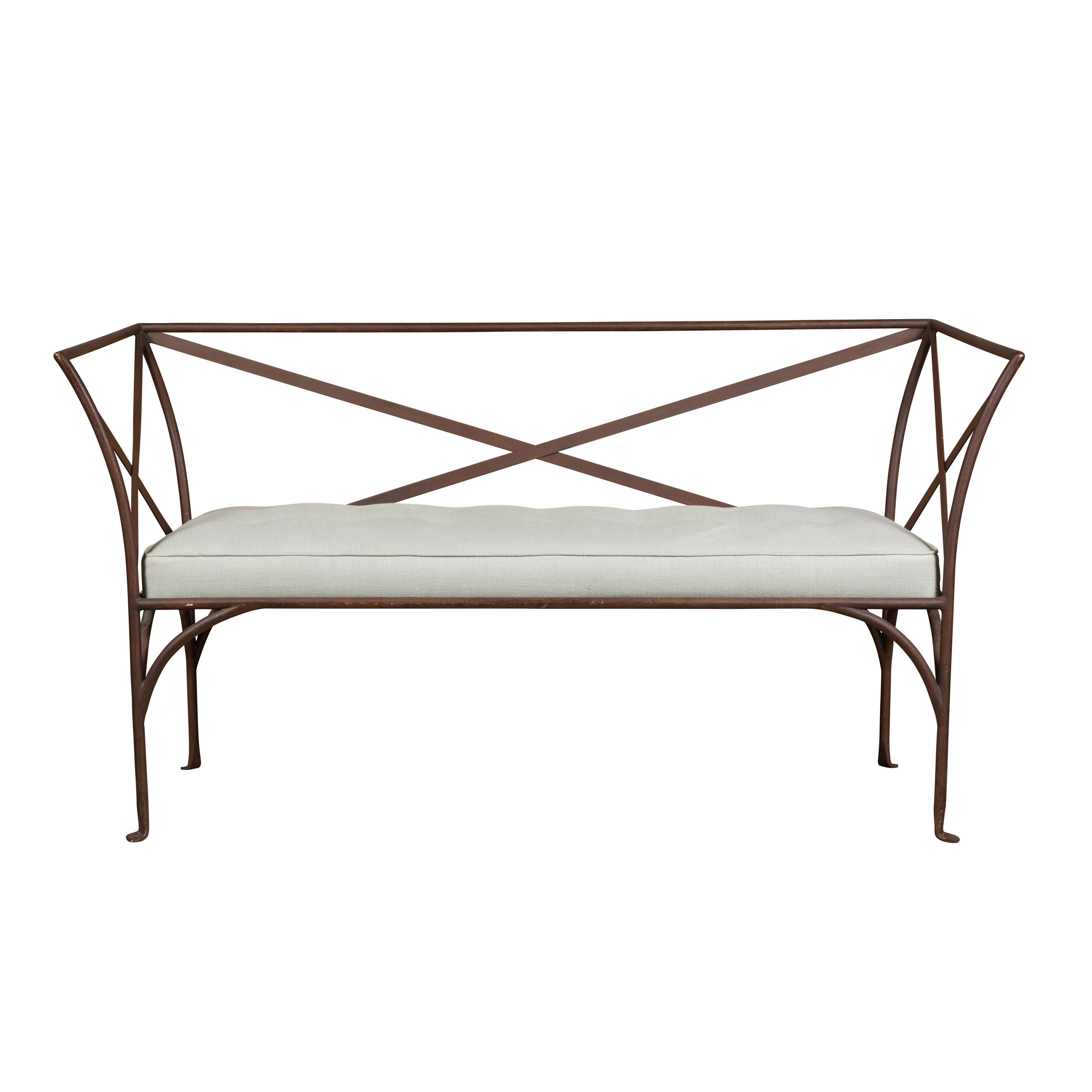 An English iron bench from the mid 20th century with out-scrolling side supports, pad feet and custom cushion. This mid-20th century English iron bench stands as a testament to both timeless design and enduring craftsmanship. Its elegant silhouette