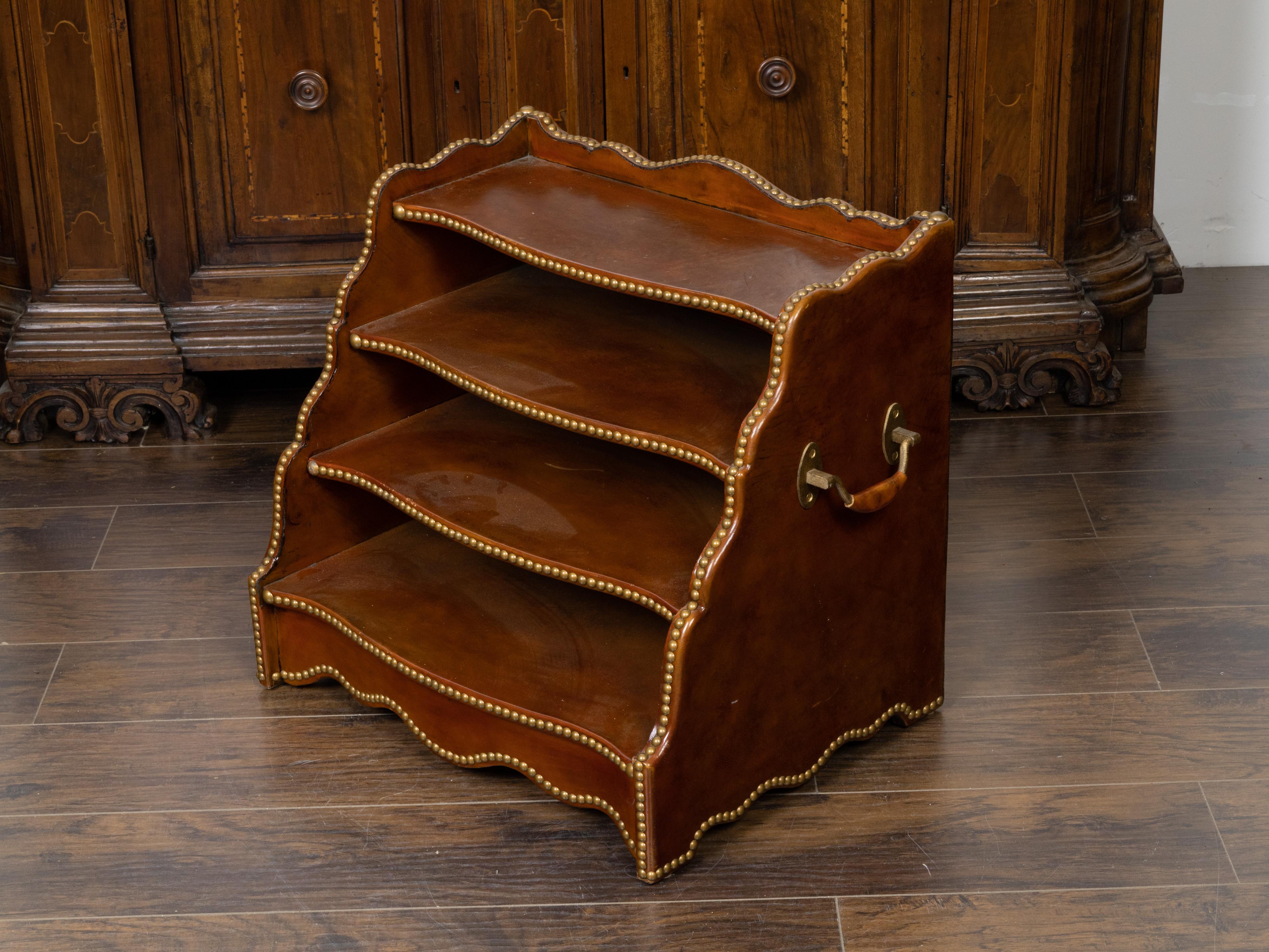 An English leather magazine rack from the mid 20h century, with four shelves and brass nailhead trim. Created in England during the midcentury period, this leather magazine rack features a scalloped silhouette flanked with waterfall style sides.