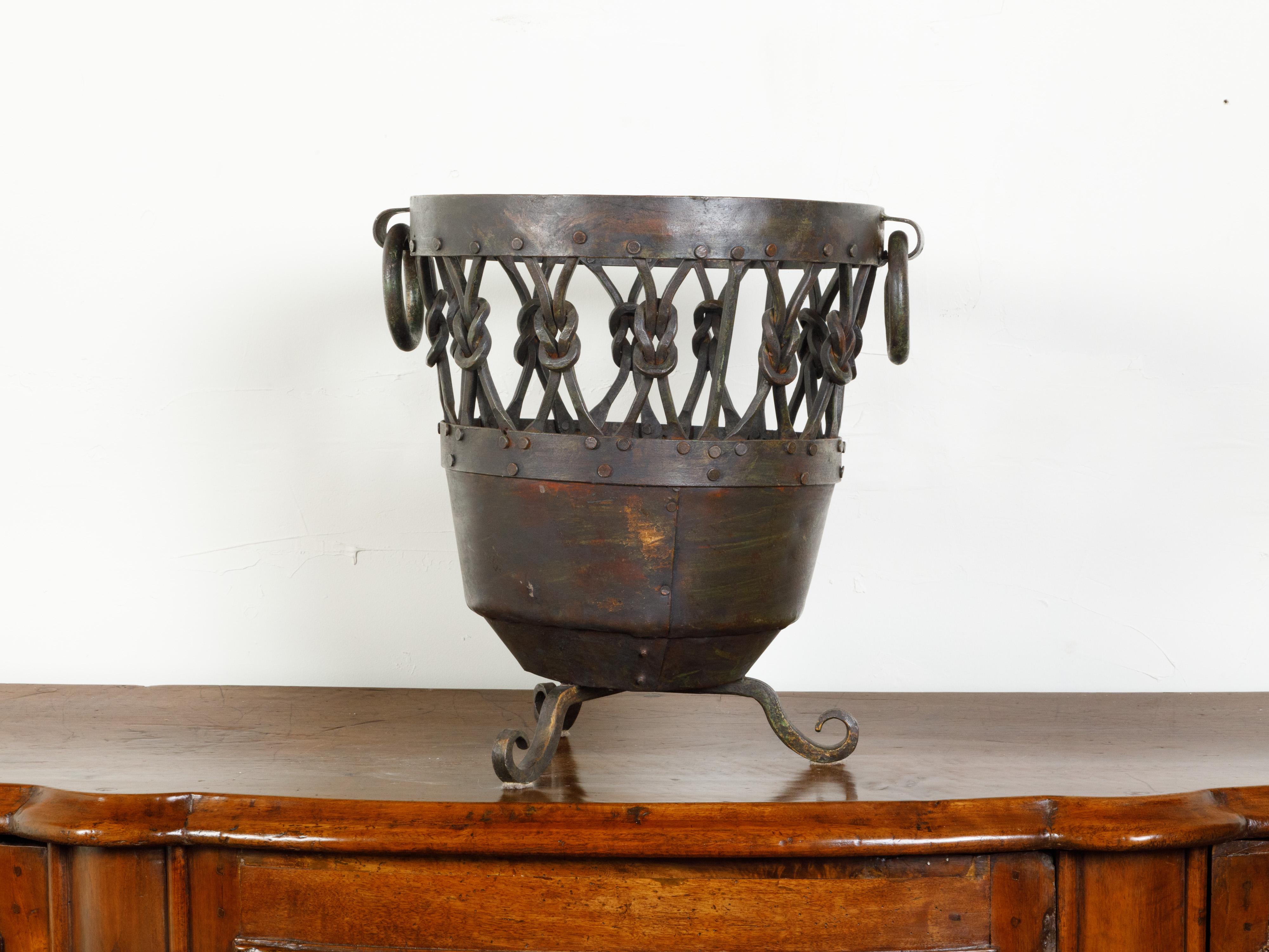 An English metal brazier /pot from the mid 20th century, with knotted motifs and scrolling feet. Created in England during the midcentury period, this metal brazier features a circular top with pierced knotted motifs, flanked with large ring pulls.