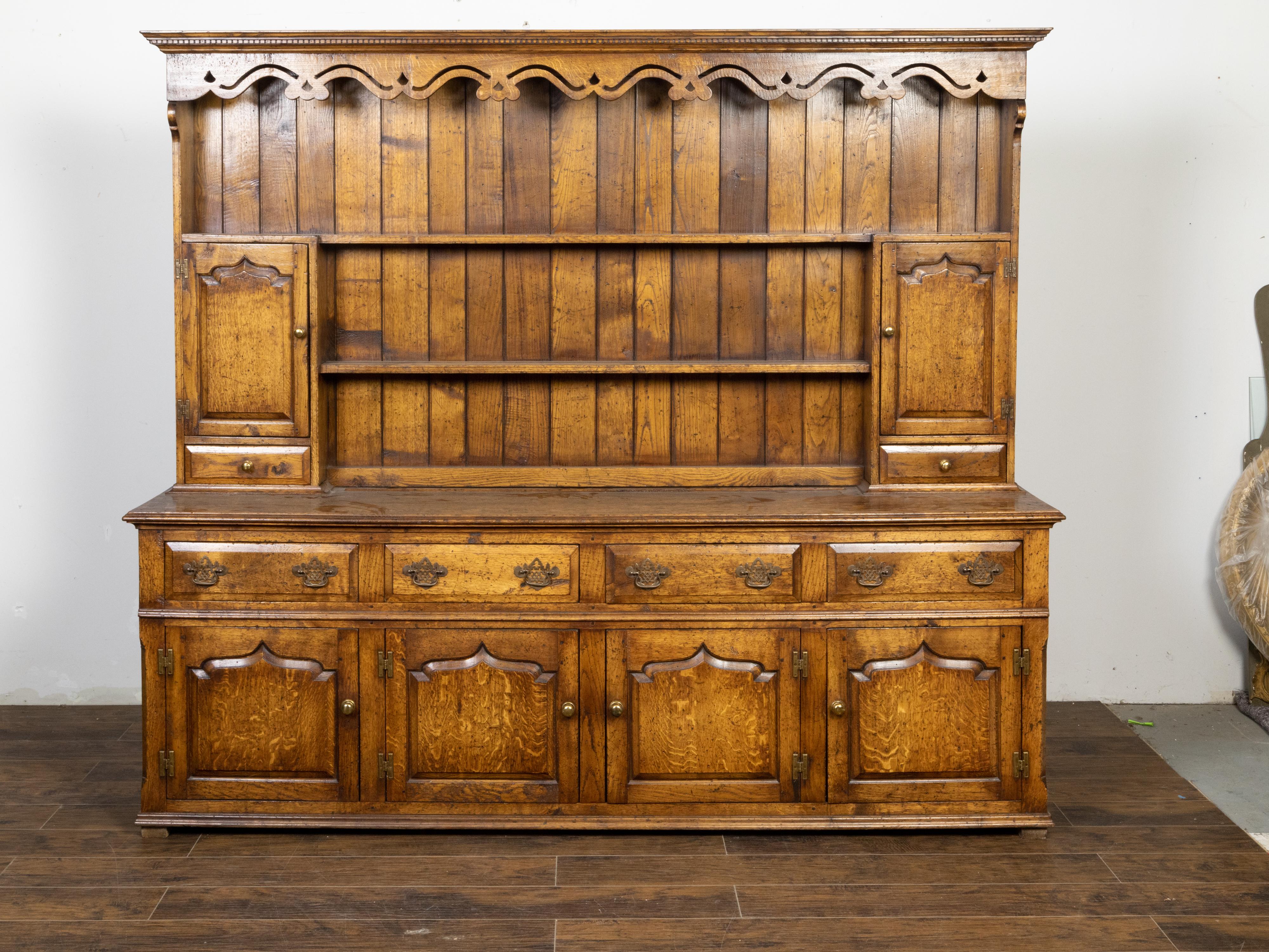 An English oak dresser from the mid 20th century, with dentil molding, carved cornice, open shelves, six doors and six drawers. Created in England during the Midcentury period, this oak dresser features a molded cornice with dentil molding and