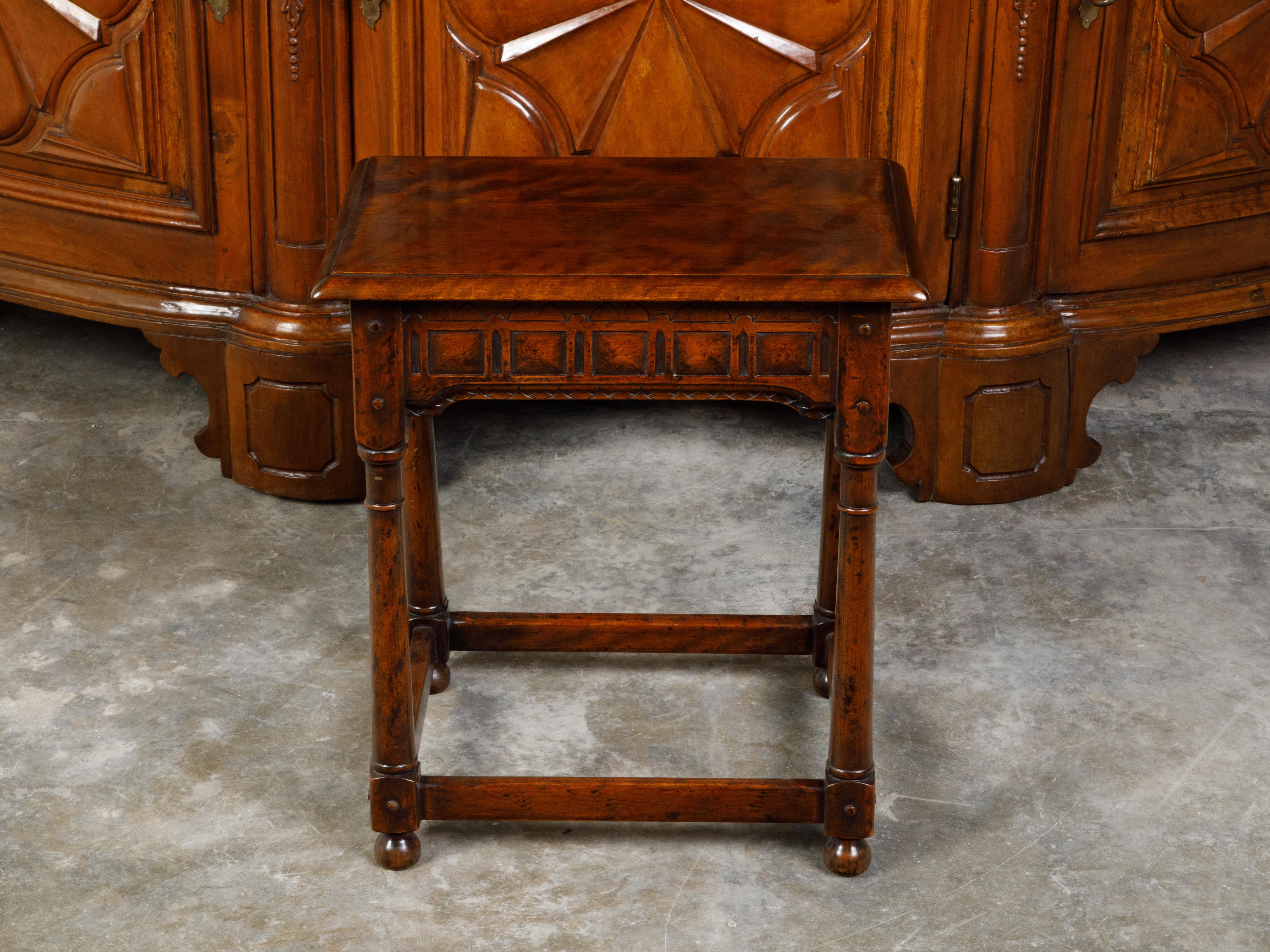 An English oak joint stool from the mid 20th century, with carved apron, turned legs and bun feet. Created in England during the Midcentury period, this oak joint stool features a rectangular top with beveled edges, sitting above an apron carved on