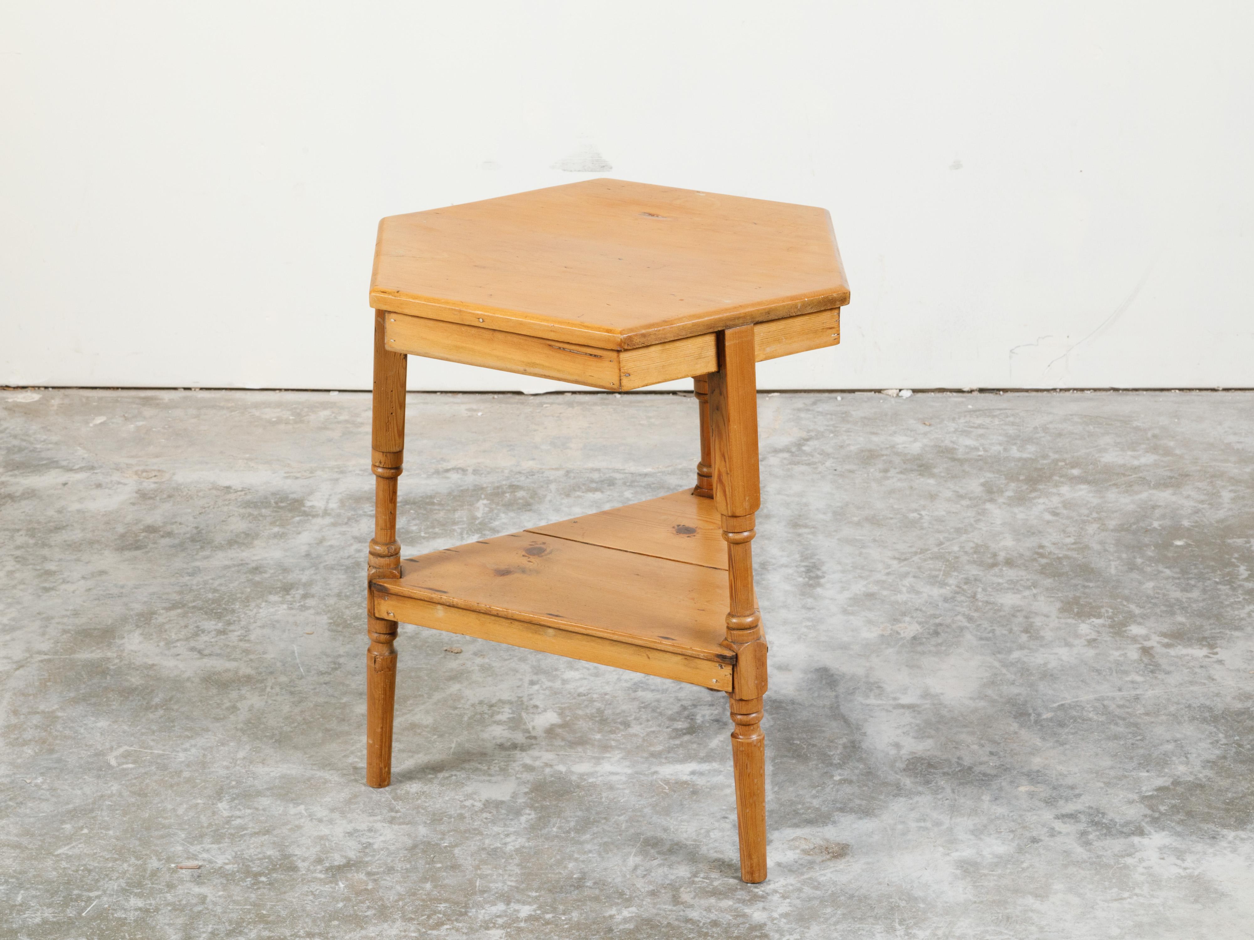 An English pine cricket table from the mid 20th century, with hexagonal top and triangular shelf. Created in England during the midcentury period, this pine table features an hexagonal top supported by three turned legs securing a lower triangular