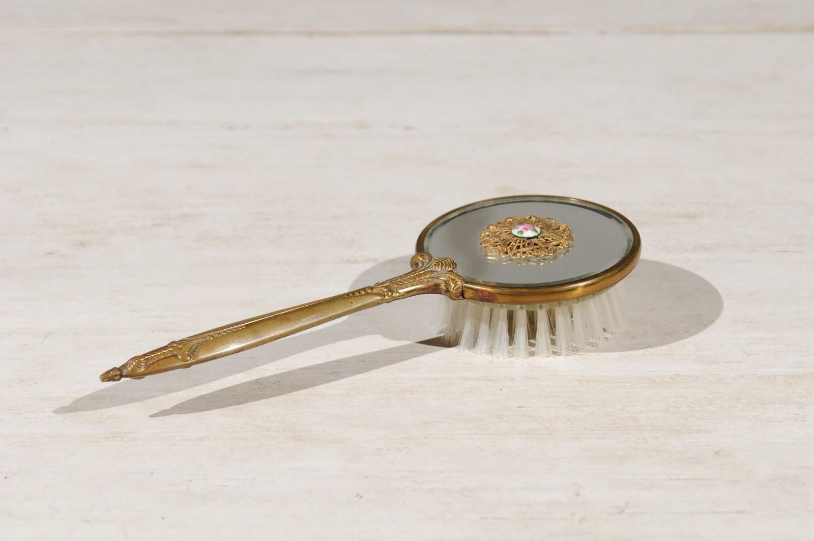 An English mirrored hair brush from the 20th century, with brass finish and filigree décor. Born in England during the 20th century, this exquisite hair brush features a circular body, mirrored on the top and accented with lovely volute motifs,