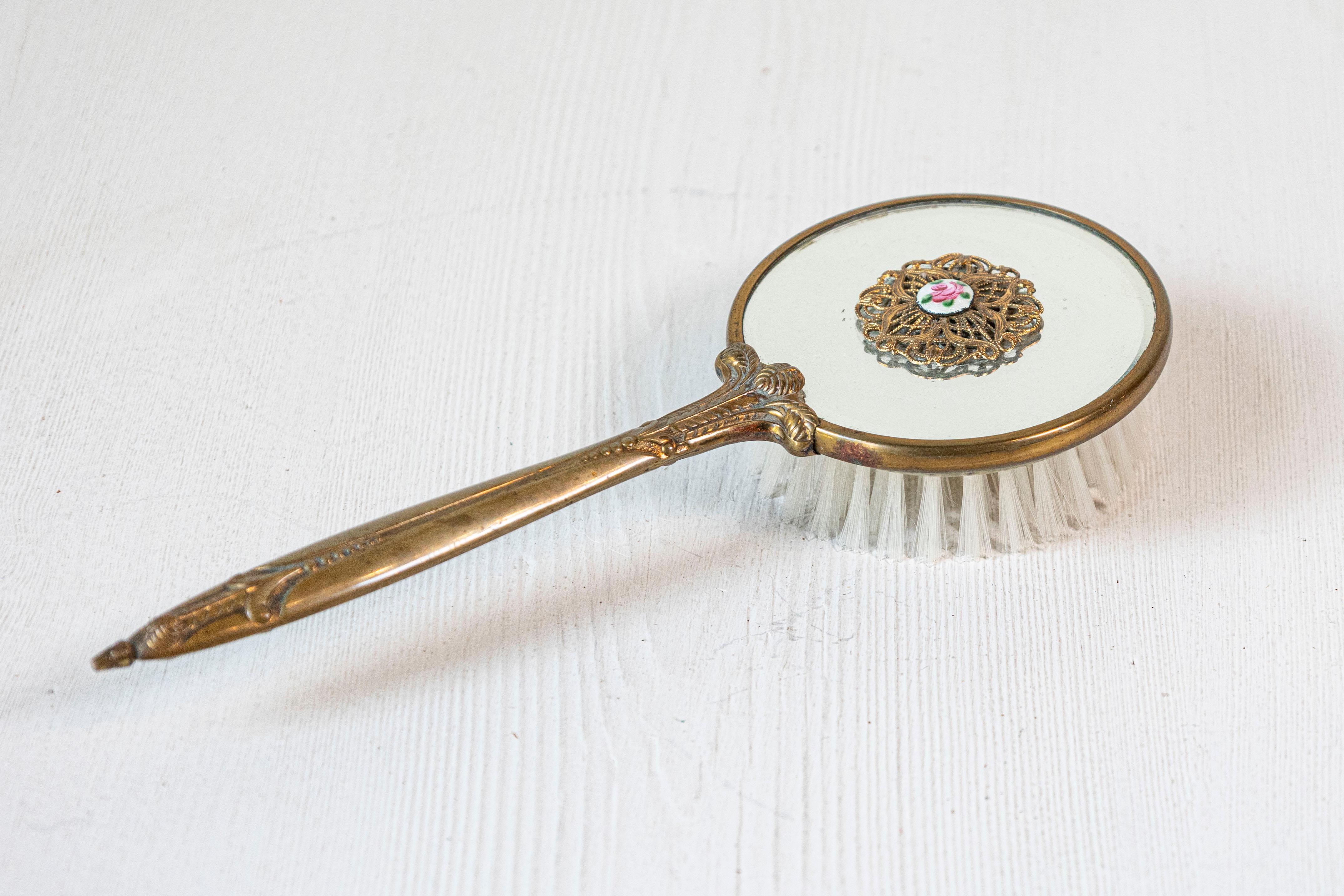 An English mirrored hair brush from the 20th century, with brass finish and filigree décor. Born in England during the 20th century, this exquisite hair brush features a circular body, mirrored on the top and accented with lovely volute motifs,