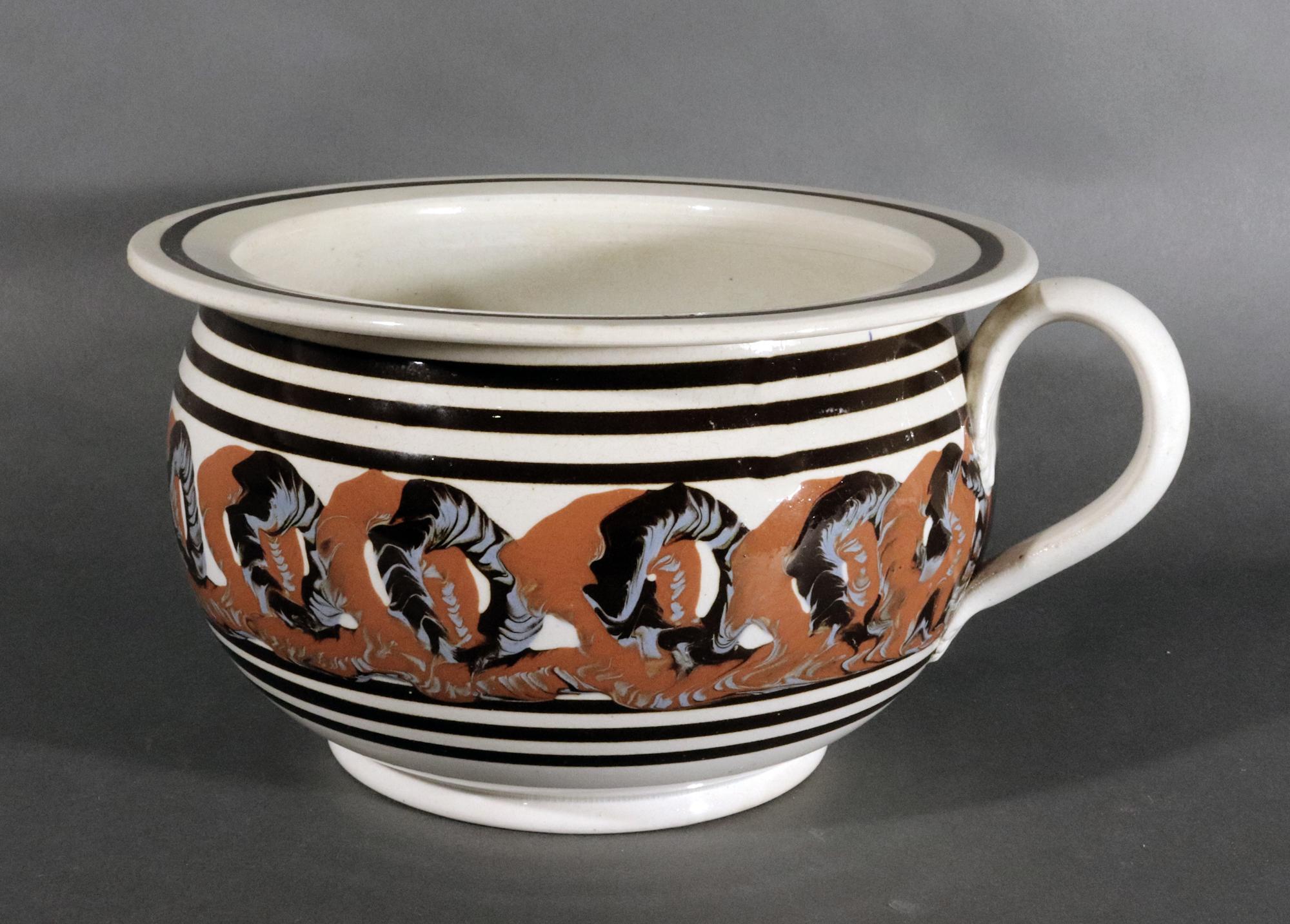 English Pottery Earthworm Mocha Chamber Pot,
Circa 1820

The circular mocha chamber pot is painted with a series of black and blue earthworm circles on a mirroring ochre red background in a band between continuous brown lines- three above and three