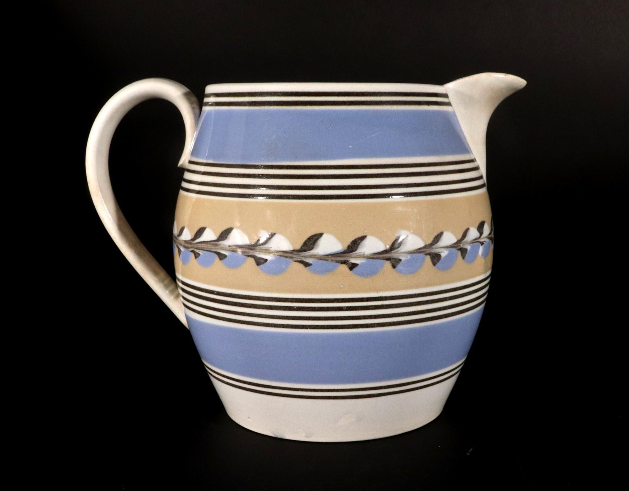 Mocha Pottery Blue & Yellow Slip Jug with Cat's eye decoration,
Early 19th Century.

This early 19th-century mocha-decorated pottery jug features a central band of yellow slip adorned with a striking tri-color cat's eye decoration. The soft yellow