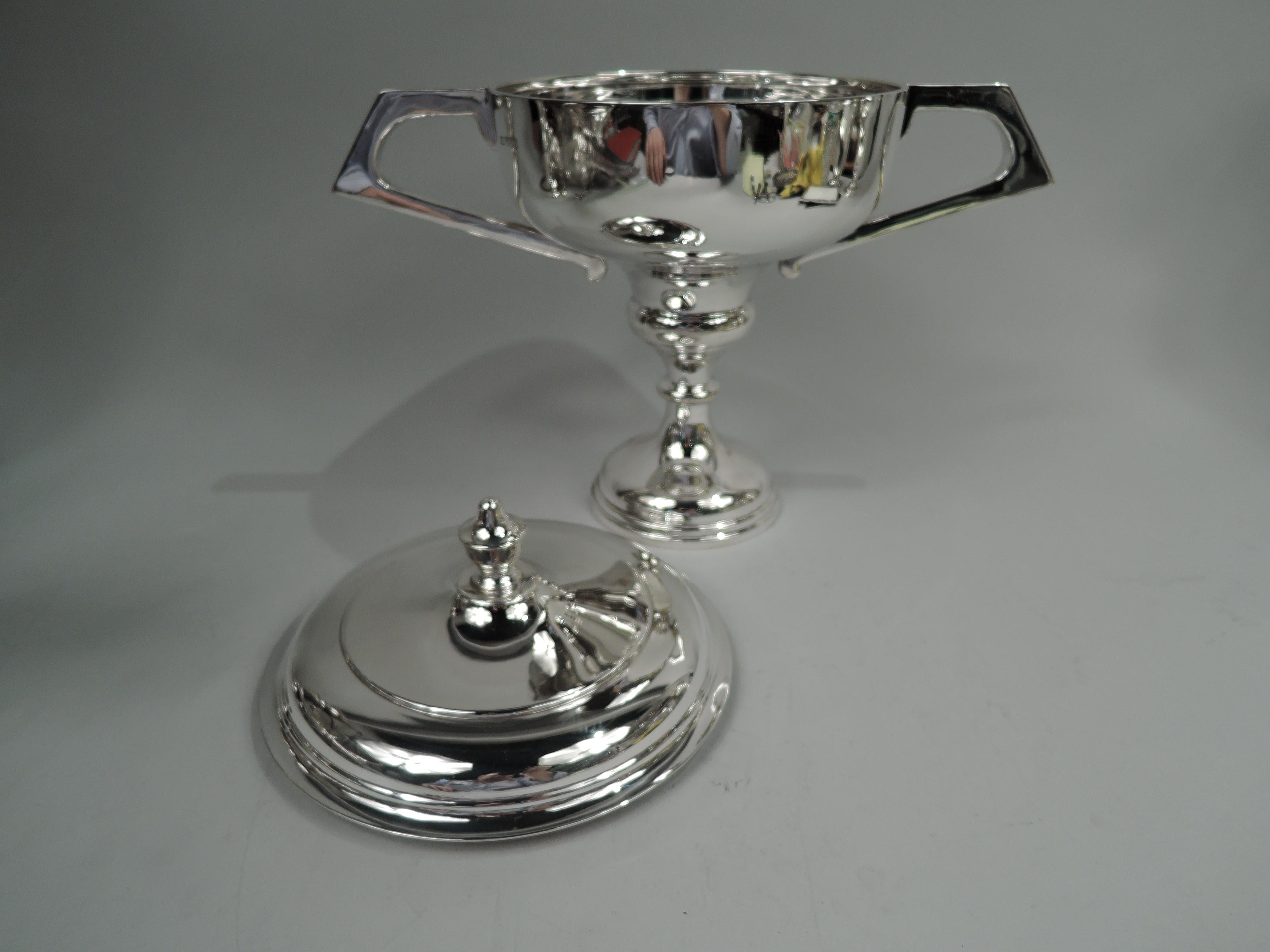 Elizabeth II sterling silver trophy cup. Made by Edward Viner in Sheffield in 1963. Wide shallow bowl with canted and elongated bracket side handles; cover raised with vasiform finial. Knopped baluster on stepped and domed foot. Fully marked.