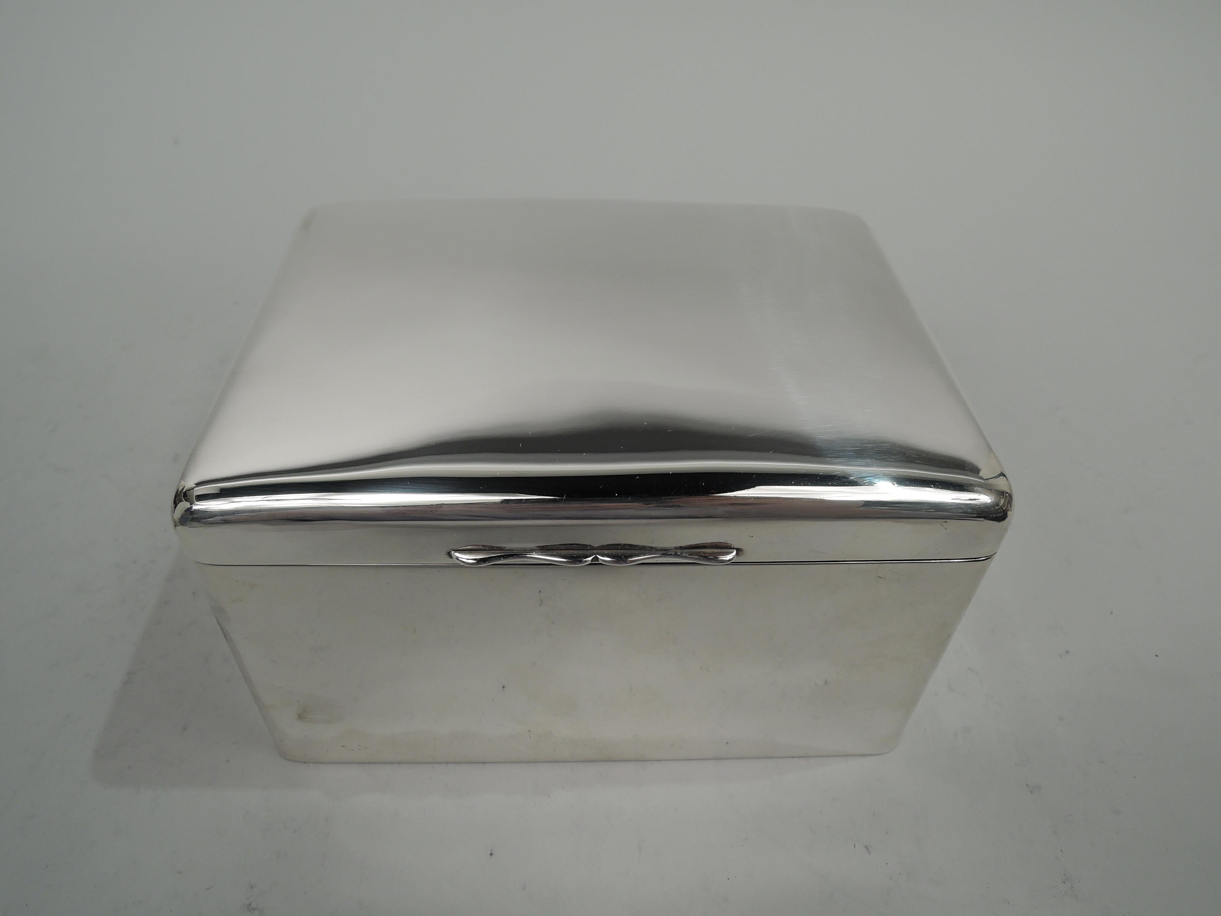 English Modern sterling silver box. Tall and rectangular with curved corners. Cover hinged with gently curved top and double-scroll tab. Box interior cedar-lined with open leather-lined bottom. Cover interior gilt. Worn marks including maker’s stamp
