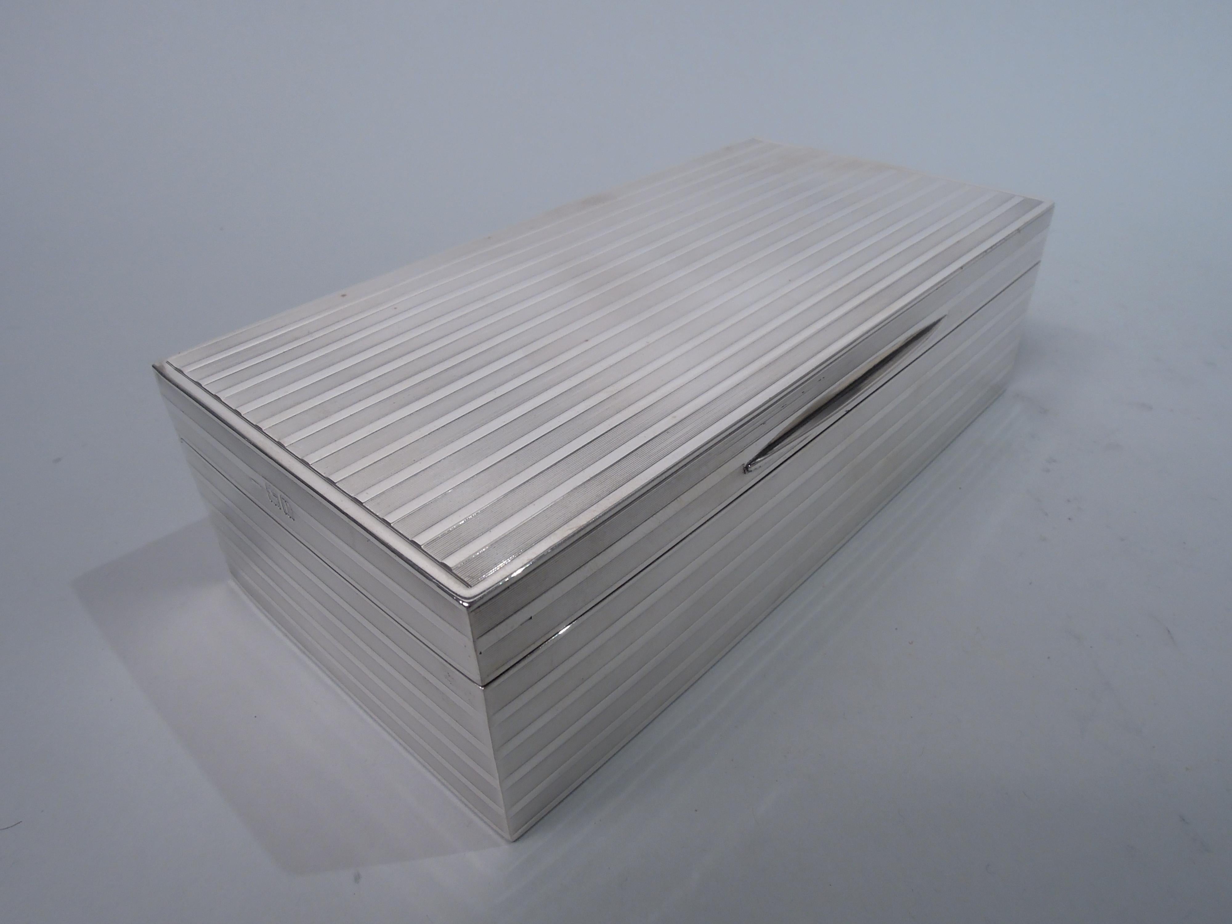 English Modern sterling silver box, 1912. Rectangular with straight sides. Cover hinged with flat top and tapering tab. Engine-turned horizontal stripes alternating with plain ones on sides and cover top. Box interior cedar-lined and partitioned and