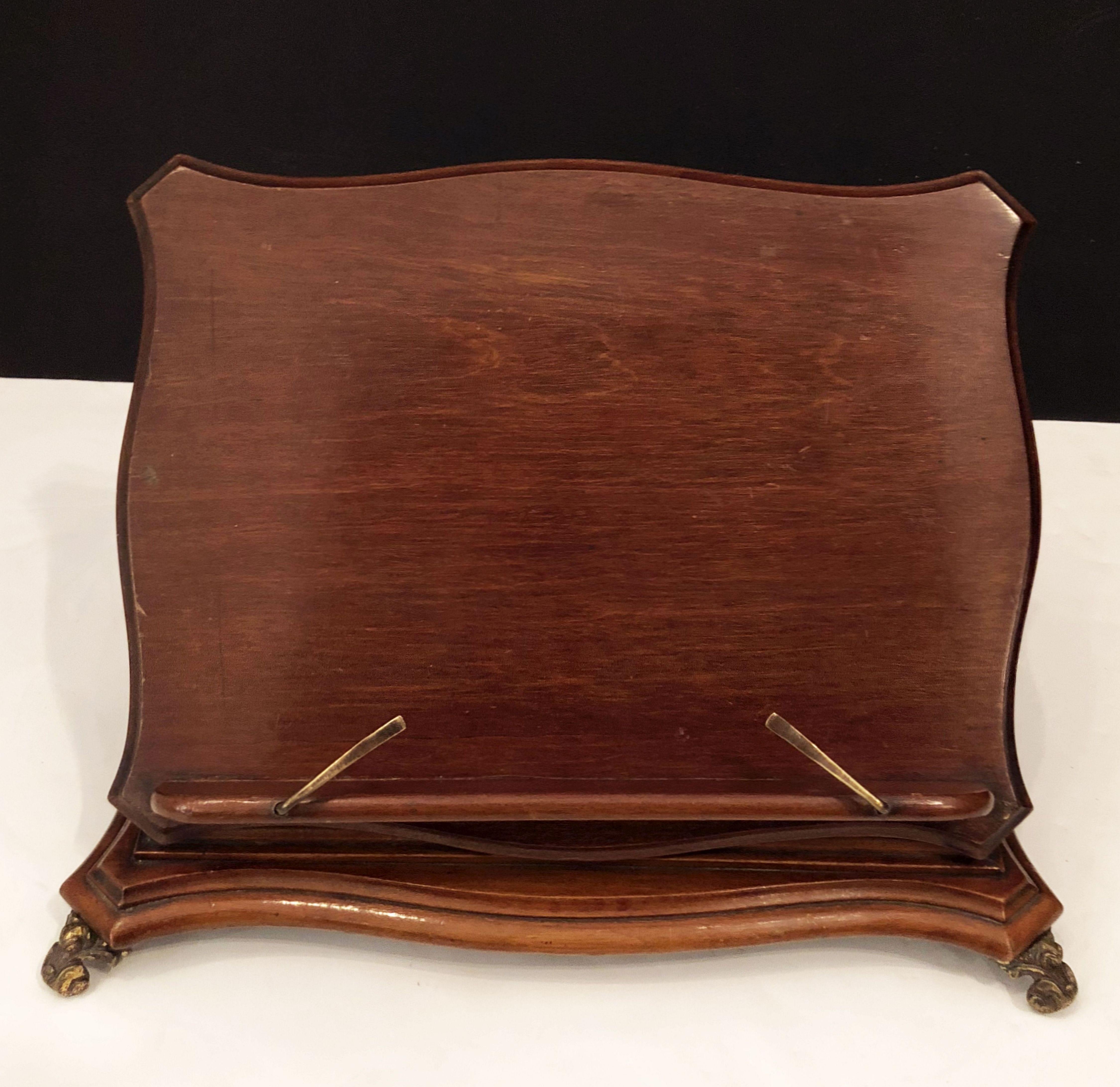 A handsome English music stand of mahogany with an elegant Art Nouveau design, featuring adjustable brass place-holders on the molded tray front and an adjustable support of brass-mounted to the molded base. Resting on brass scroll feet.

With