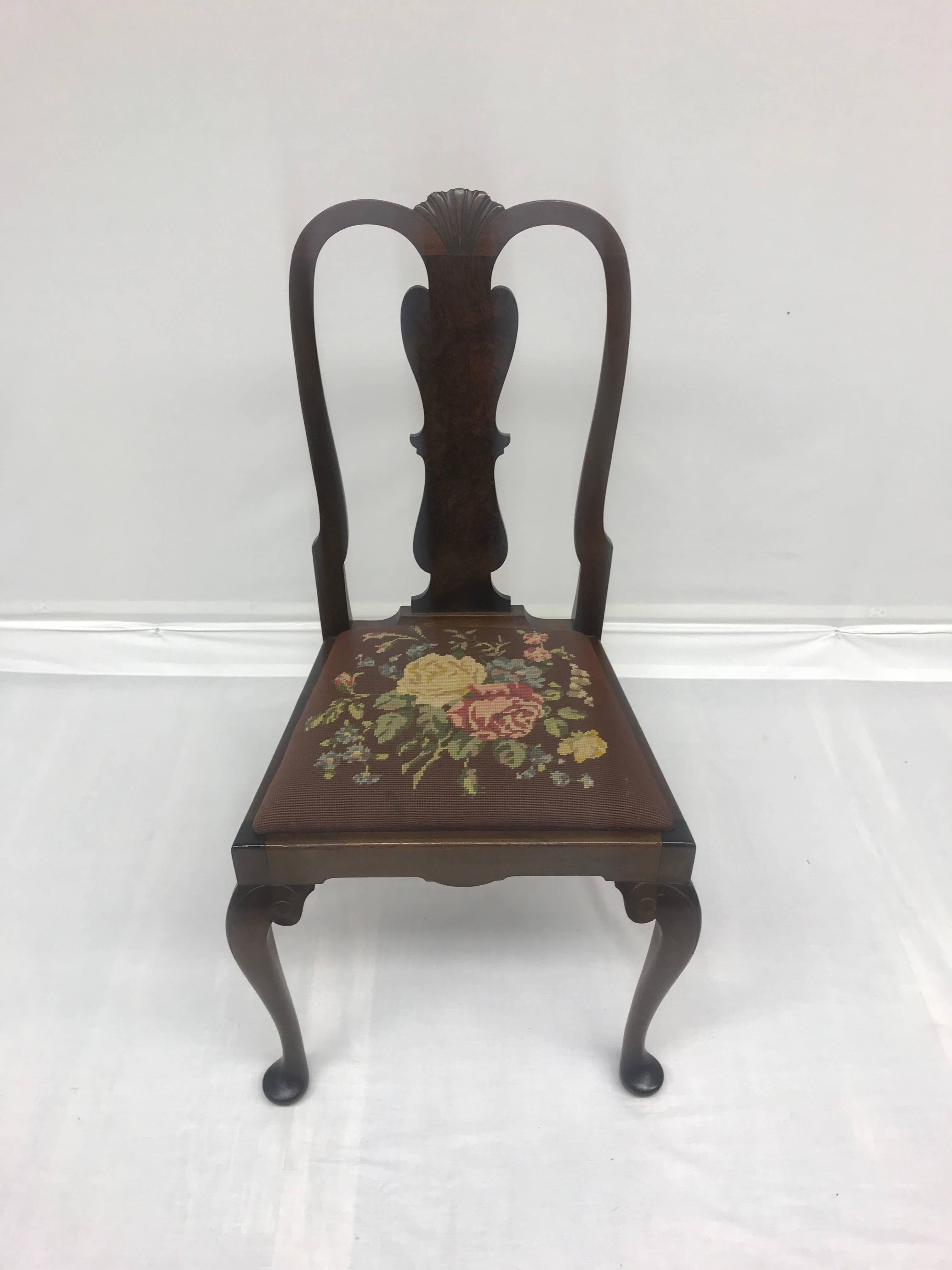 A set of four early 20th century Queen Anne-style dining chairs with seats upholstered in vintage needlepoint floral motifs. Use them around a game table or dining table or as extra seating in a front hall. The chair frames feature a dark mahogany