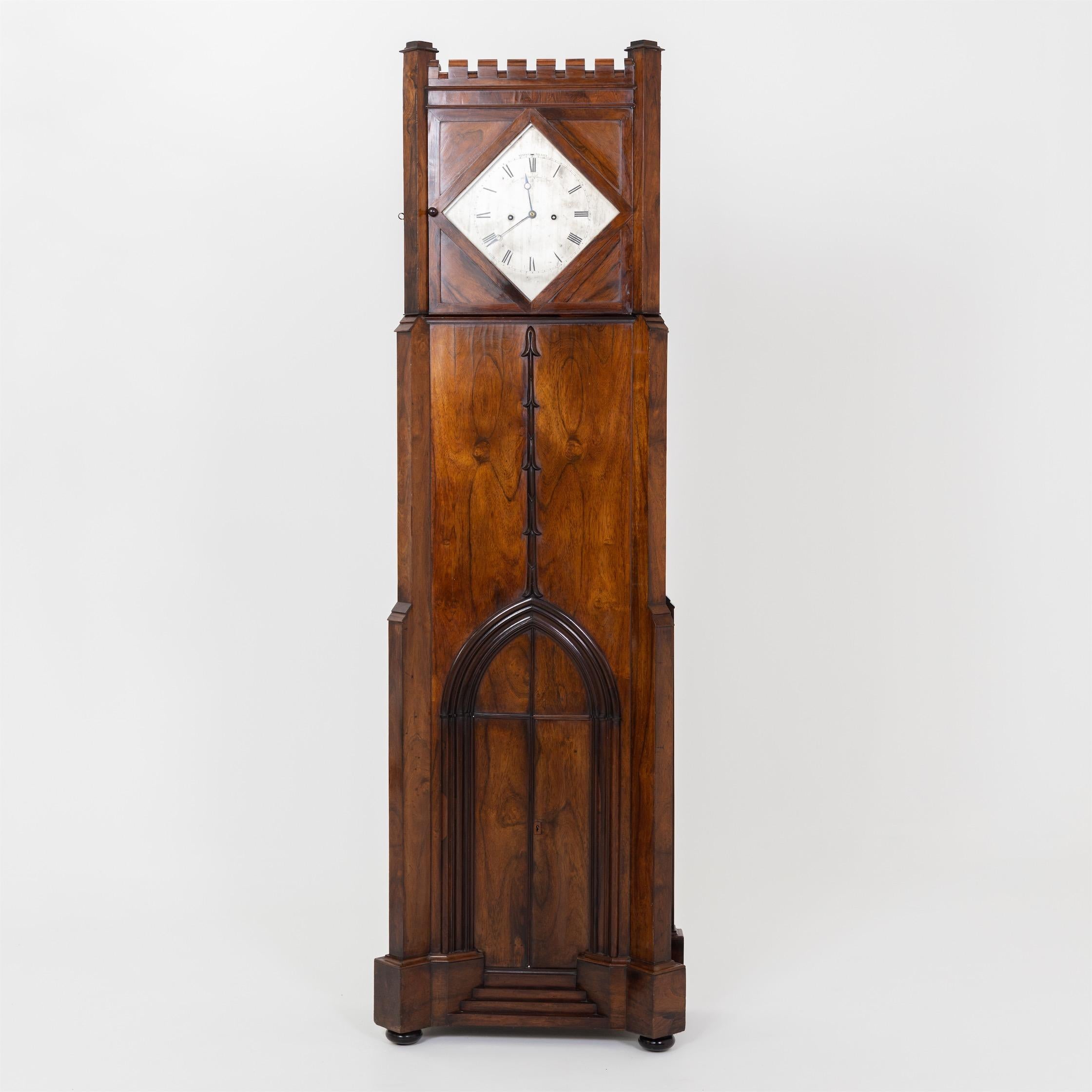 Large tower-shaped grandfather clock with crenellations and openwork tracery windows on the sides, second half of the 19th century. The diamond-shaped window reveals the clock face with Roman numerals, inscribed “Payne 163 New Bond Street”. Payne &
