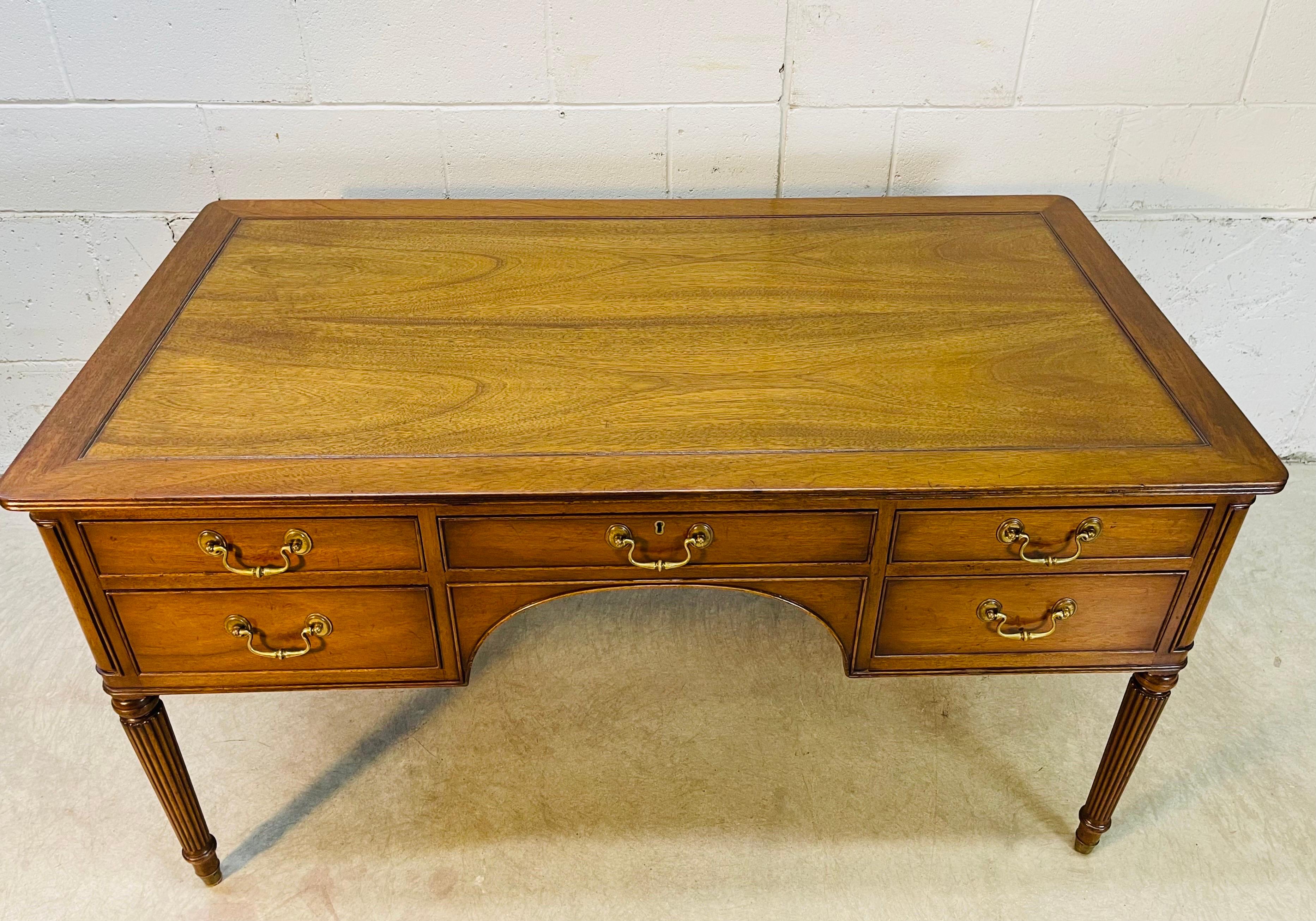 Vintage 1940s Neoclassical English Sheraton style mahogany desk by Kittinger. The desk has five drawers for storage. The pulls are solid brass and the legs are a tapered column style. The wood is solid and in excellent refinished condition. The knee
