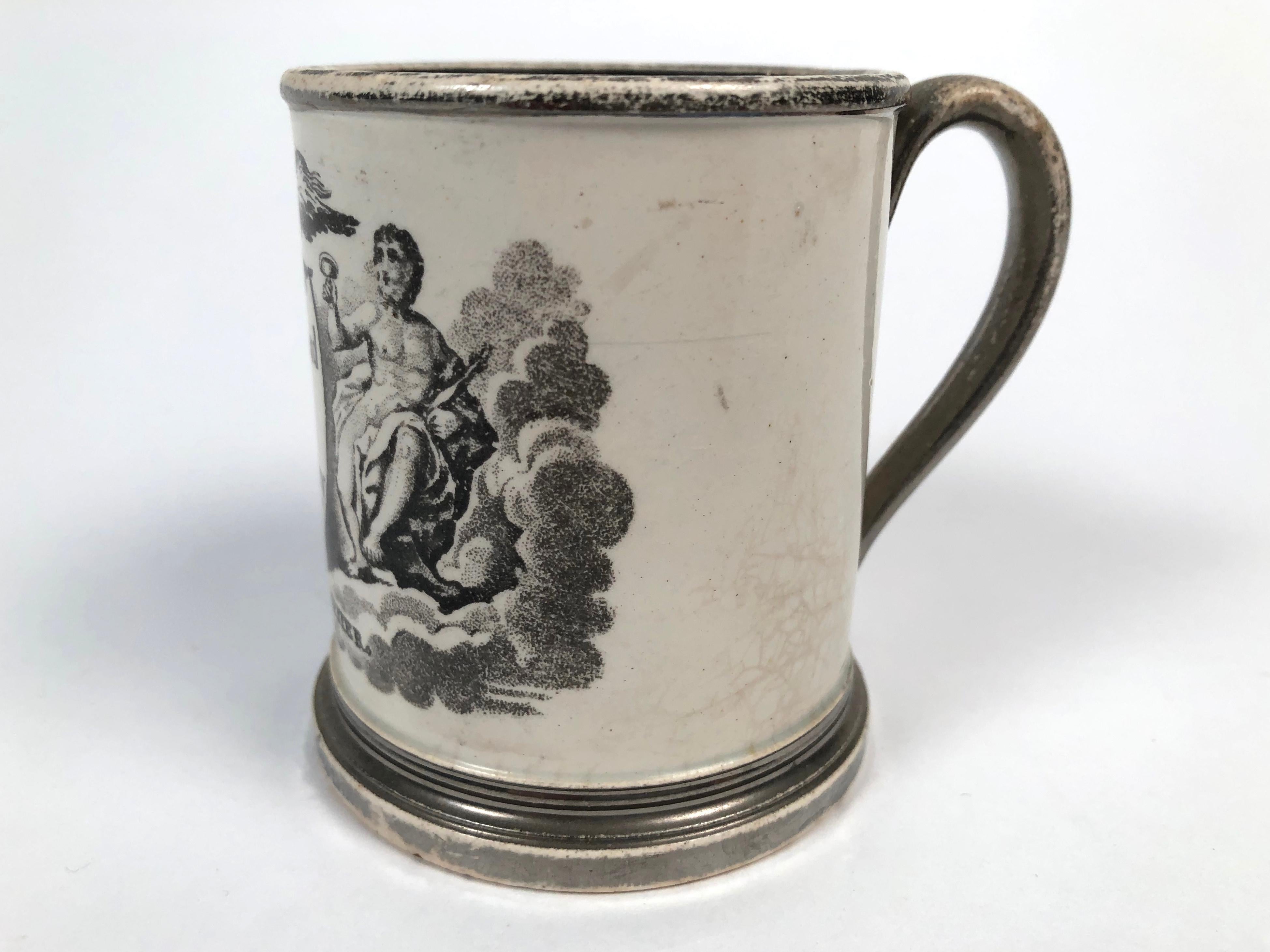 A small English neoclassical Staffordshire black transfeware pottery cup with the words a reward for Industry printed on a shield, in the center, surmounted by an eagle and flanked, on the left, by Hebe, holding a vessel, and, on the right, Jupiter