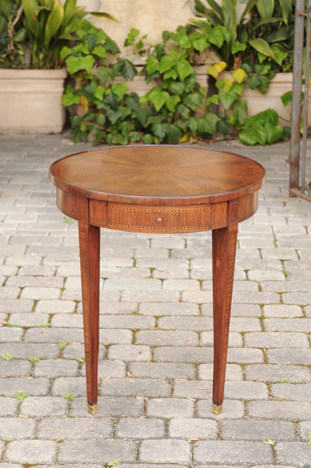 An English neoclassical style mahogany guéridon side table from the early 20th century, with inlaid accents, single drawer and radiating veneer. Born in England during the early years of the 20th century, this exquisite Edwardian side table features