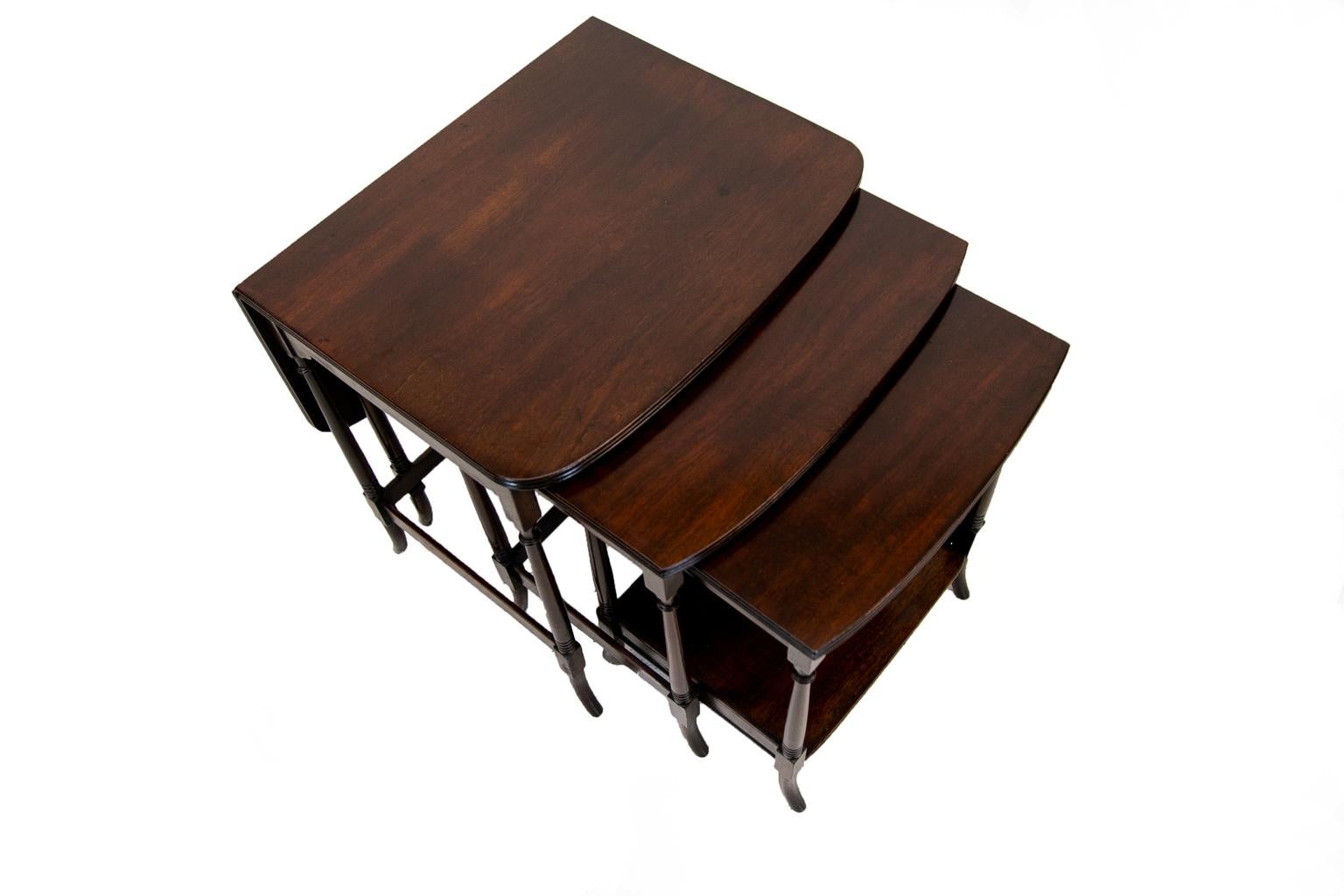 This English nest of three tables is solid mahogany. The smallest table has a shelf with a three sided gallery. All three tables have tripled reeded edges. The largest table has a rear drop leaf that can be raised if desired, and is supported by a