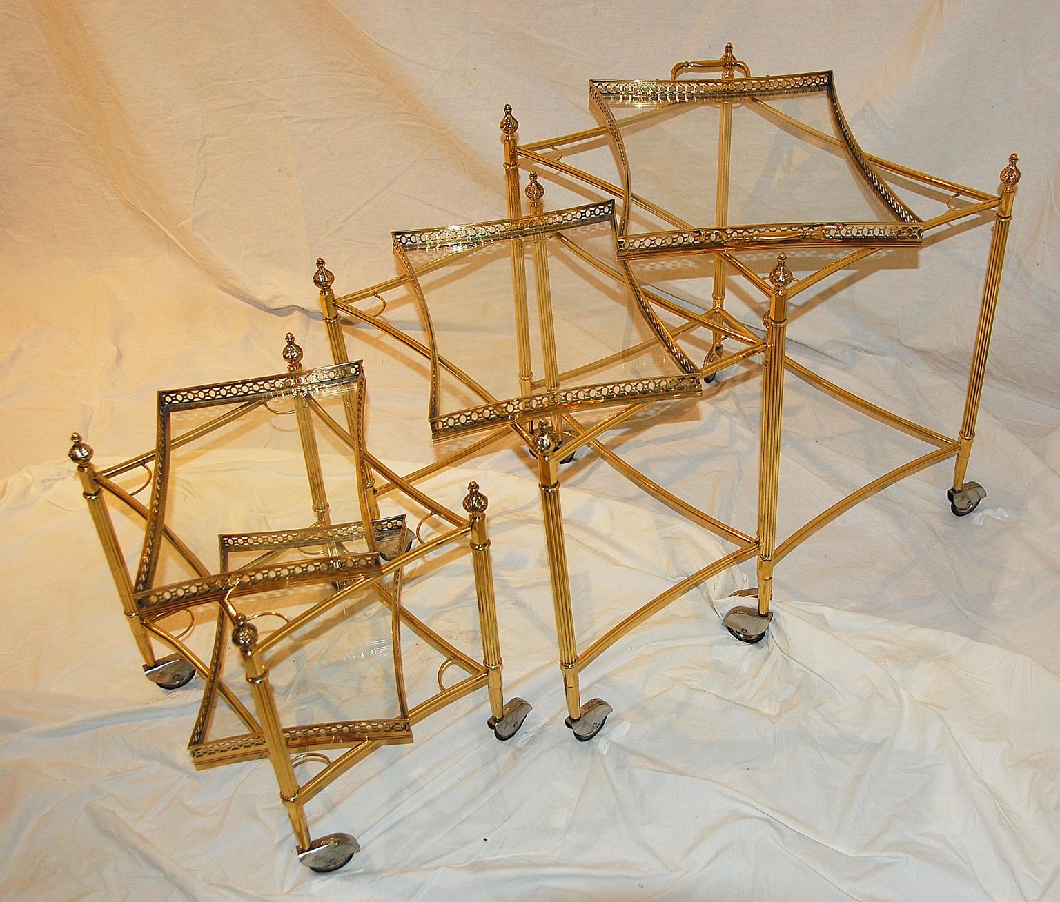 English nesting set of three brass bar carts with removable galleried brass and glass trays. The three carts are rectangular with graceful concave sides. The galleries of each tray are pierced, the smallest cart having two trays, the other two