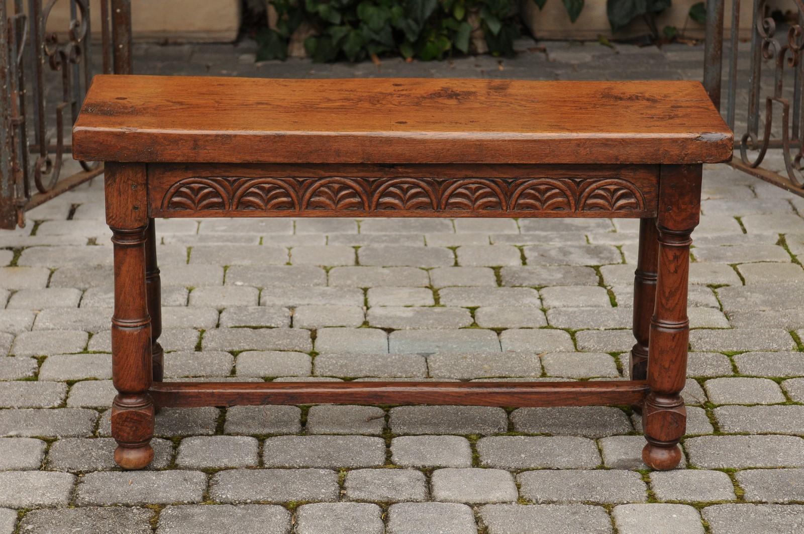 An English oak bench from the late 19th century, with low-relief carved decor, column-shaped turned legs and cross stretcher. Born in England towards the end of the 19th century, this oak bench distinguishes itself with its rectangular top and