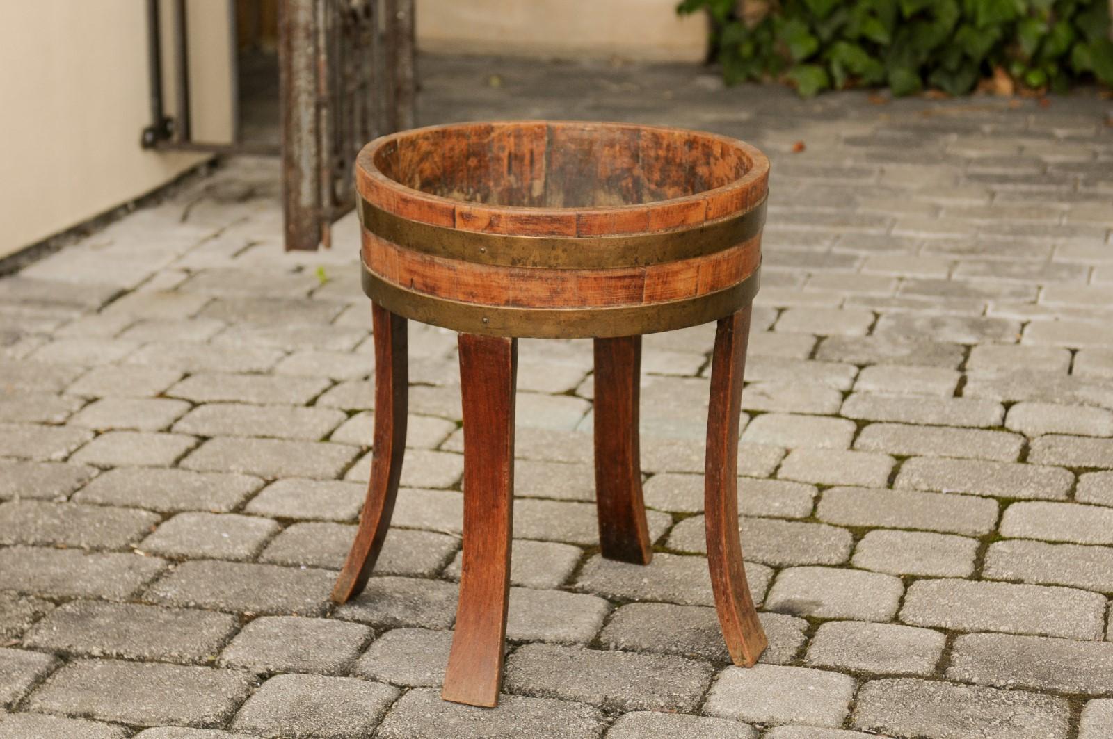 An English oak circular planter from the late 19th century, with later legs and brass accents. Born during the fourth quarter of the 19th century, this rustic oak planter features a circular body, accented with brass braces. The planter is mounted
