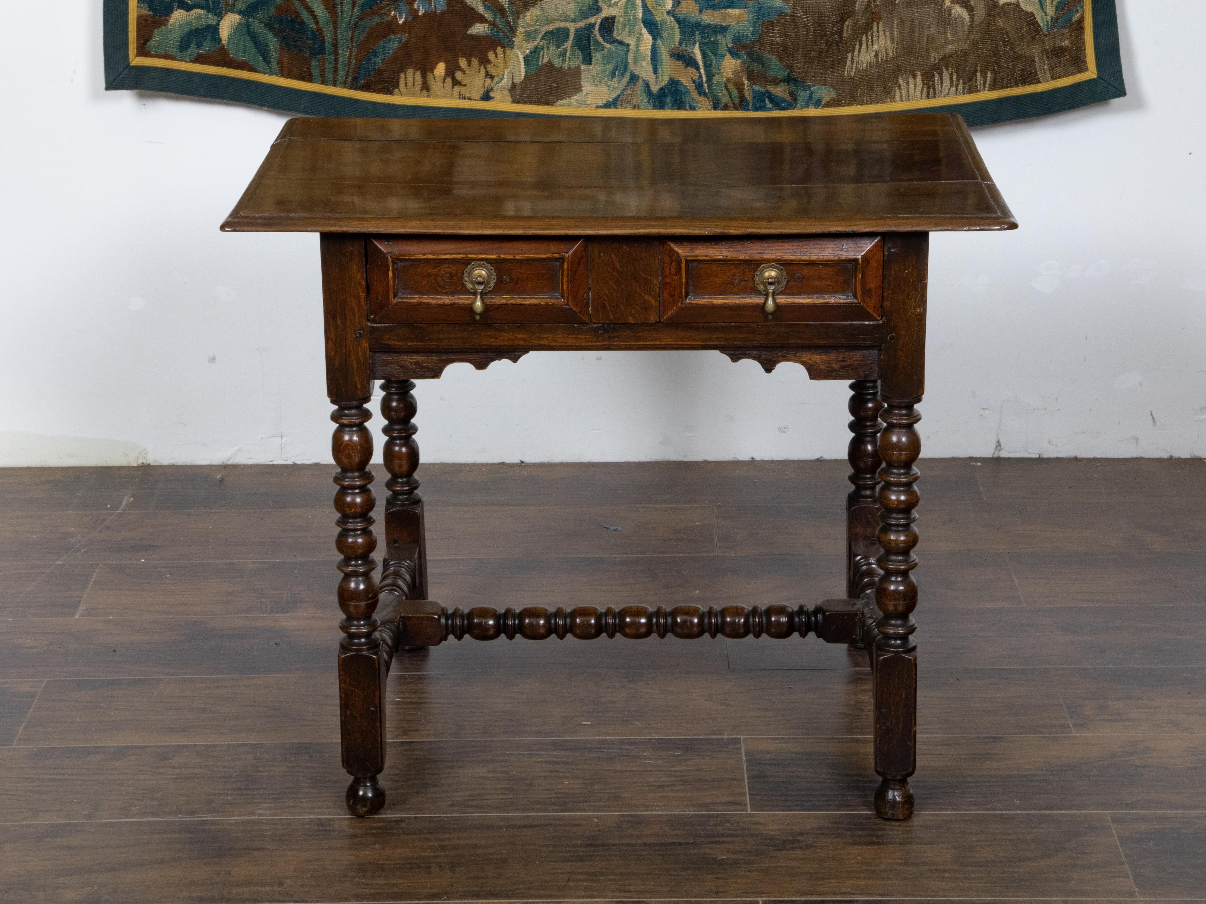 An English carved geometric front oak side table from the 19th century, with single drawer, bobbin legs, H-form cross stretcher and brass hardware. Created in England during the 19th century, this oak side table features a rectangular planked top