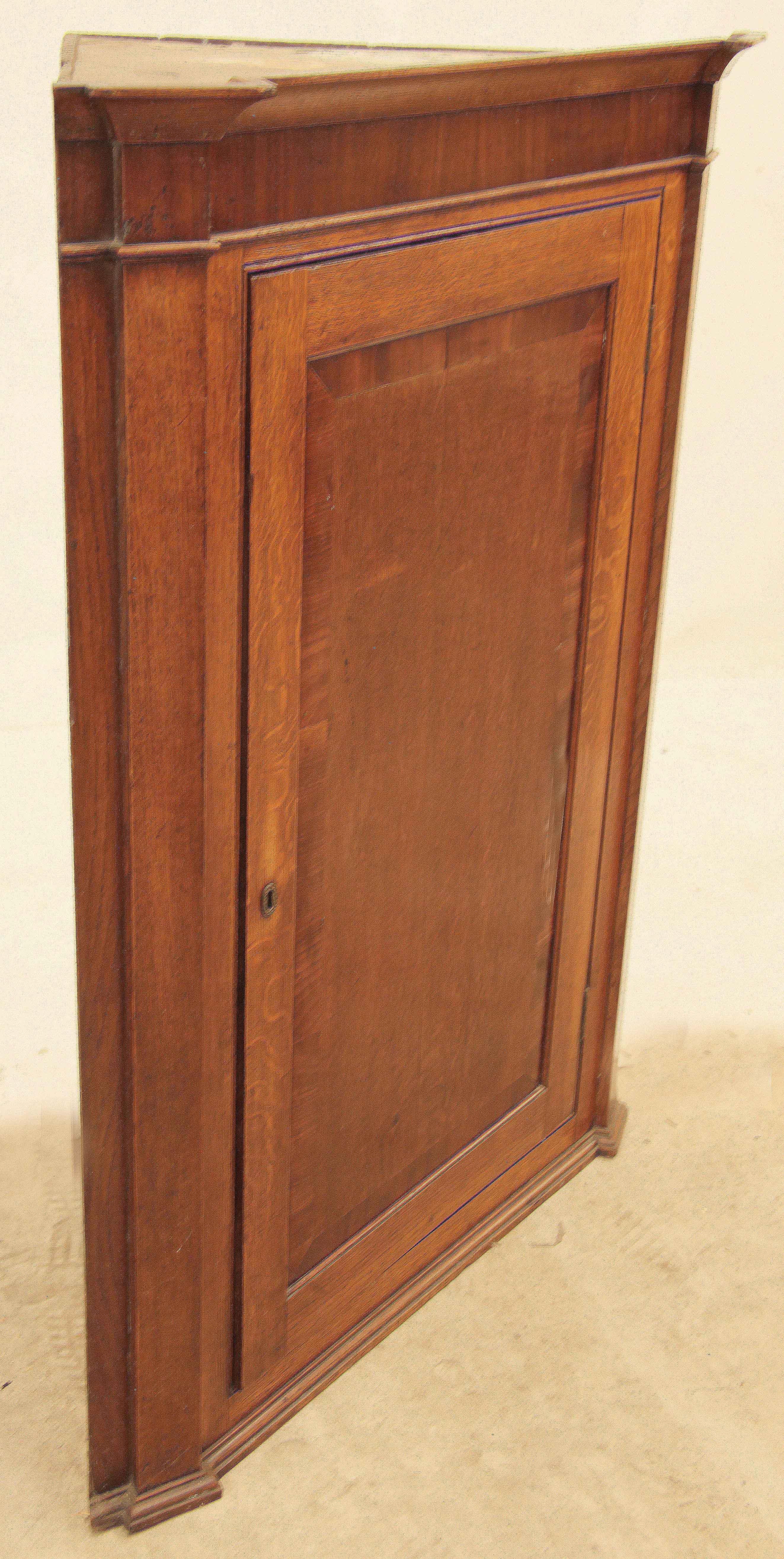 Armadio angolare sospeso in Oak e mogano,  Sotto il cornicione è presente un fregio impiallacciato in mogano.  Le stele ''scoppiano''  che è una caratteristica insolita e attraente.  L'anta singola è a fasce incrociate in mogano e si apre per